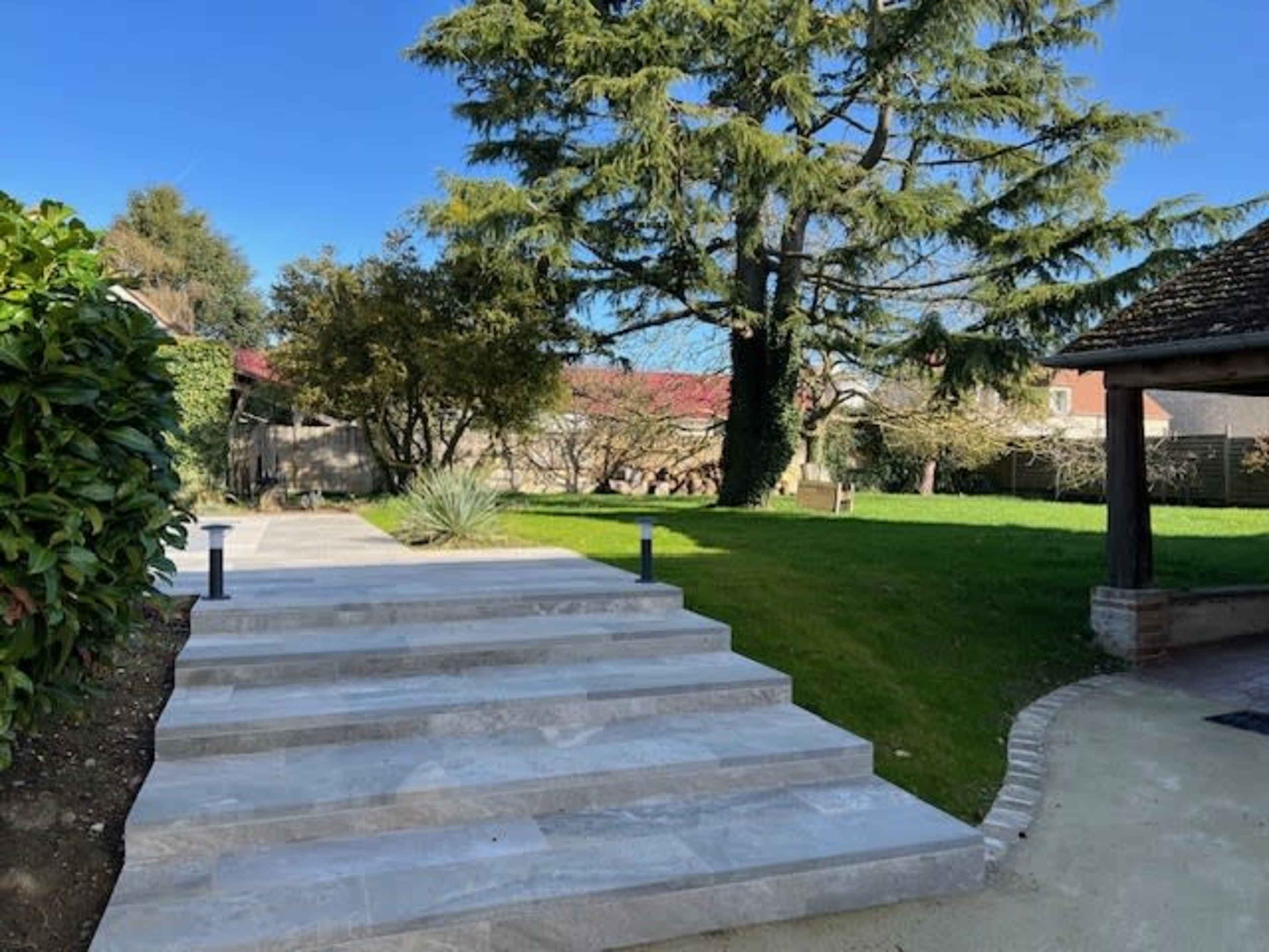 The image shows a landscaped yard featuring stone steps leading to a green lawn surrounded by trees and shrubs.