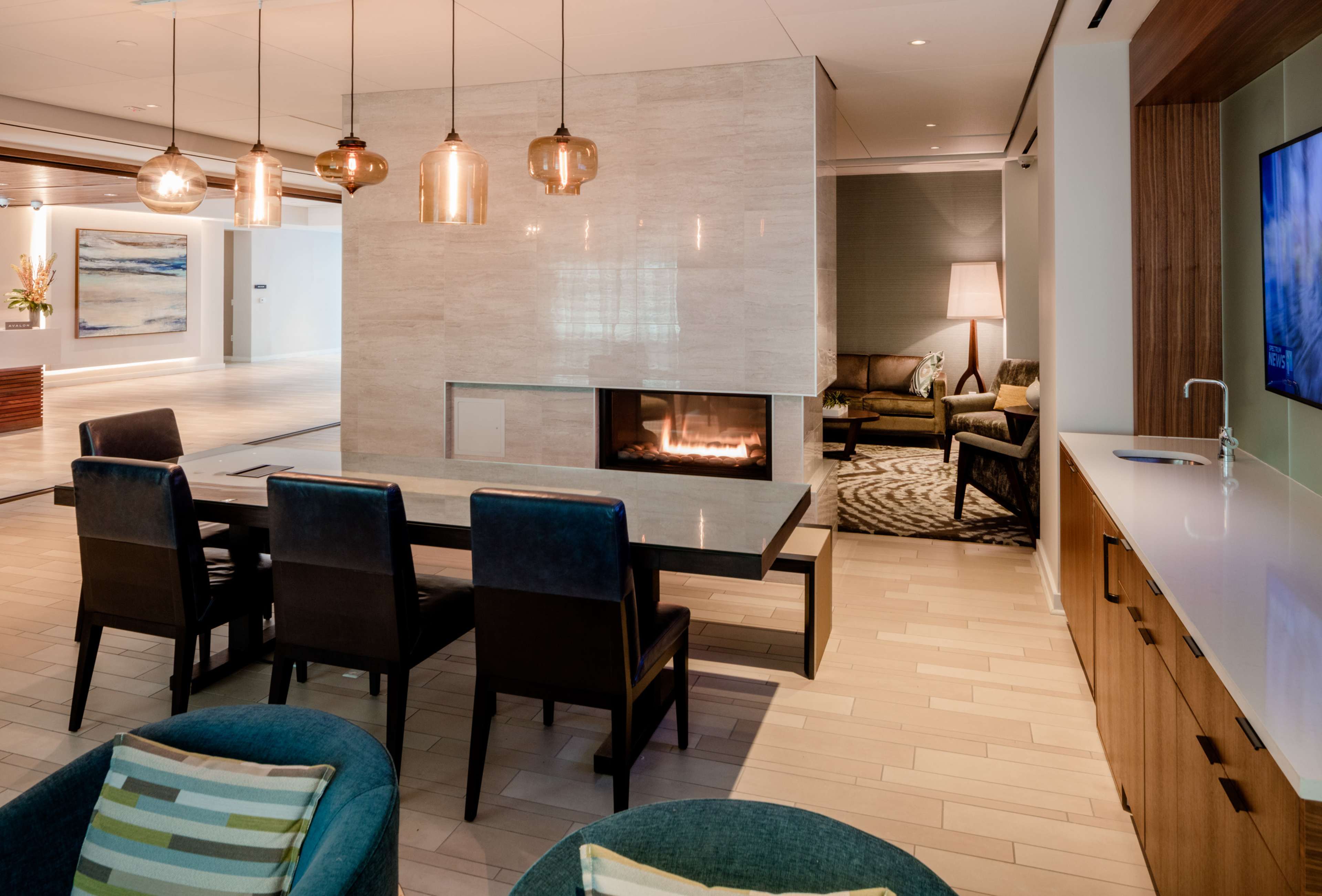 The image shows a modern lounge area with a fireplace, a dining table, and stylish seating arrangements, accented by pendant lights and a television.