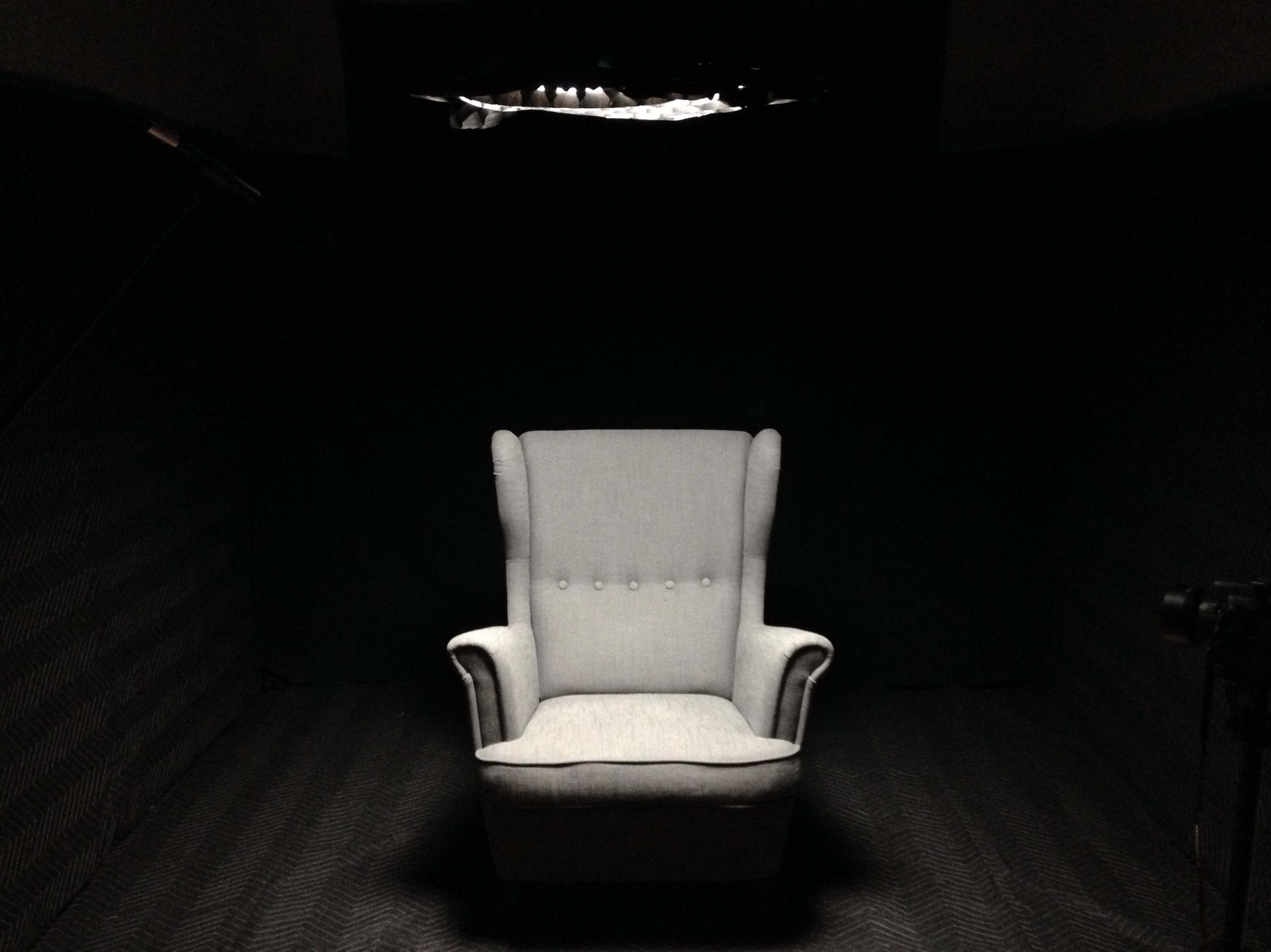 A single, light-colored armchair is centered in a dark room with soundproof walls.
