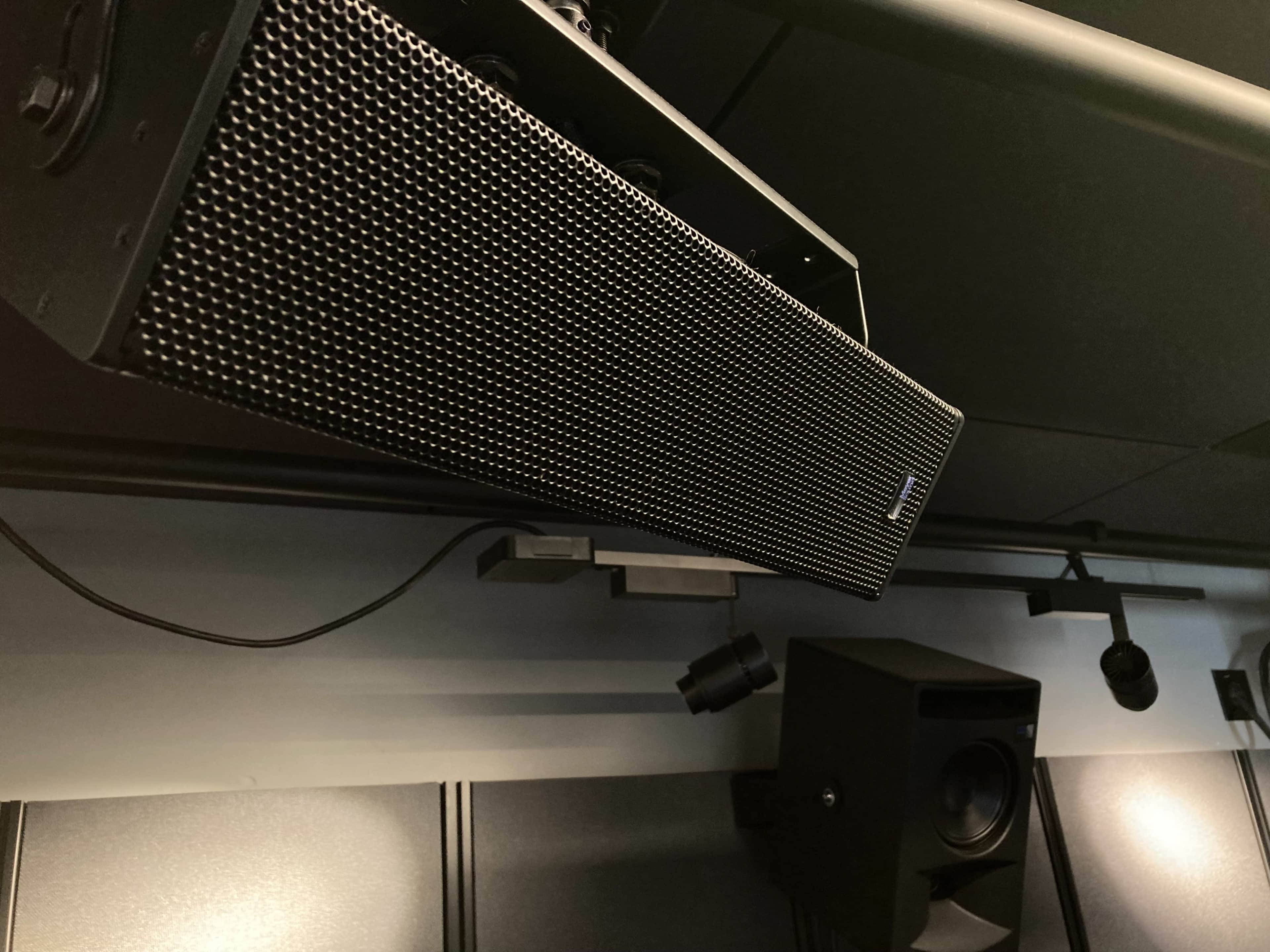 The image shows two audio speakers mounted on a ceiling, with one long speaker positioned horizontally and another smaller speaker located beneath it.
