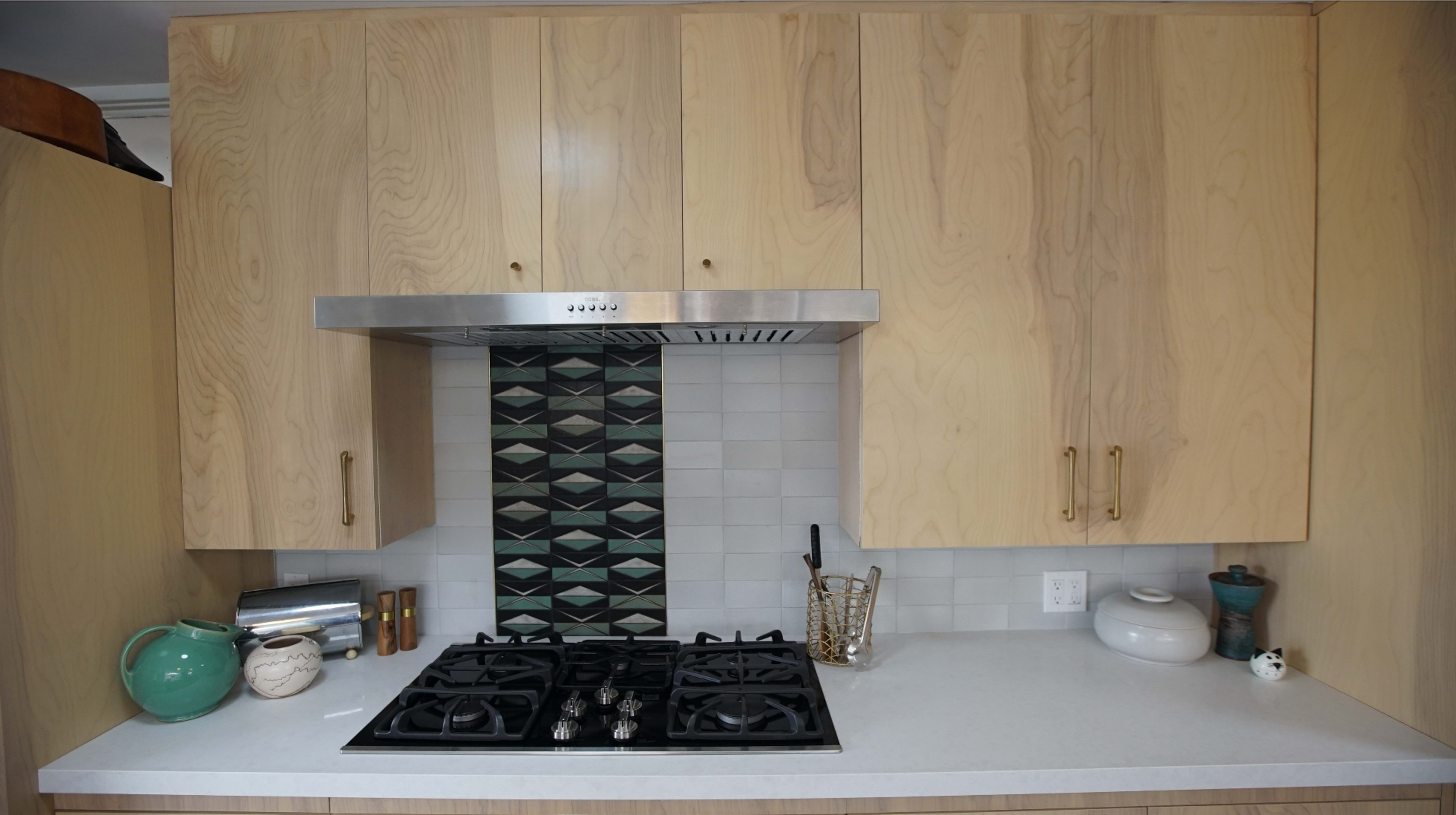 A modern kitchen with wooden cabinetry, a stainless steel range hood, a gas cooktop, and a patterned backsplash.