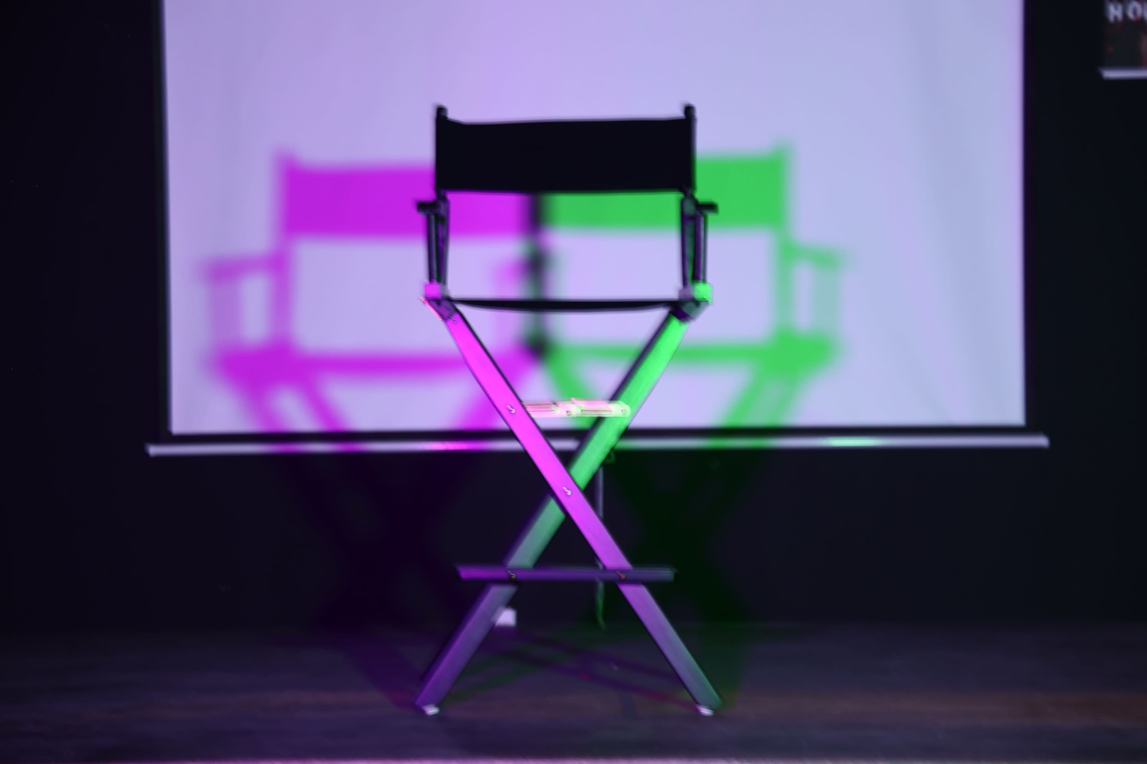 A director's chair is positioned in front of a projected screen, casting colorful shadows on the floor.