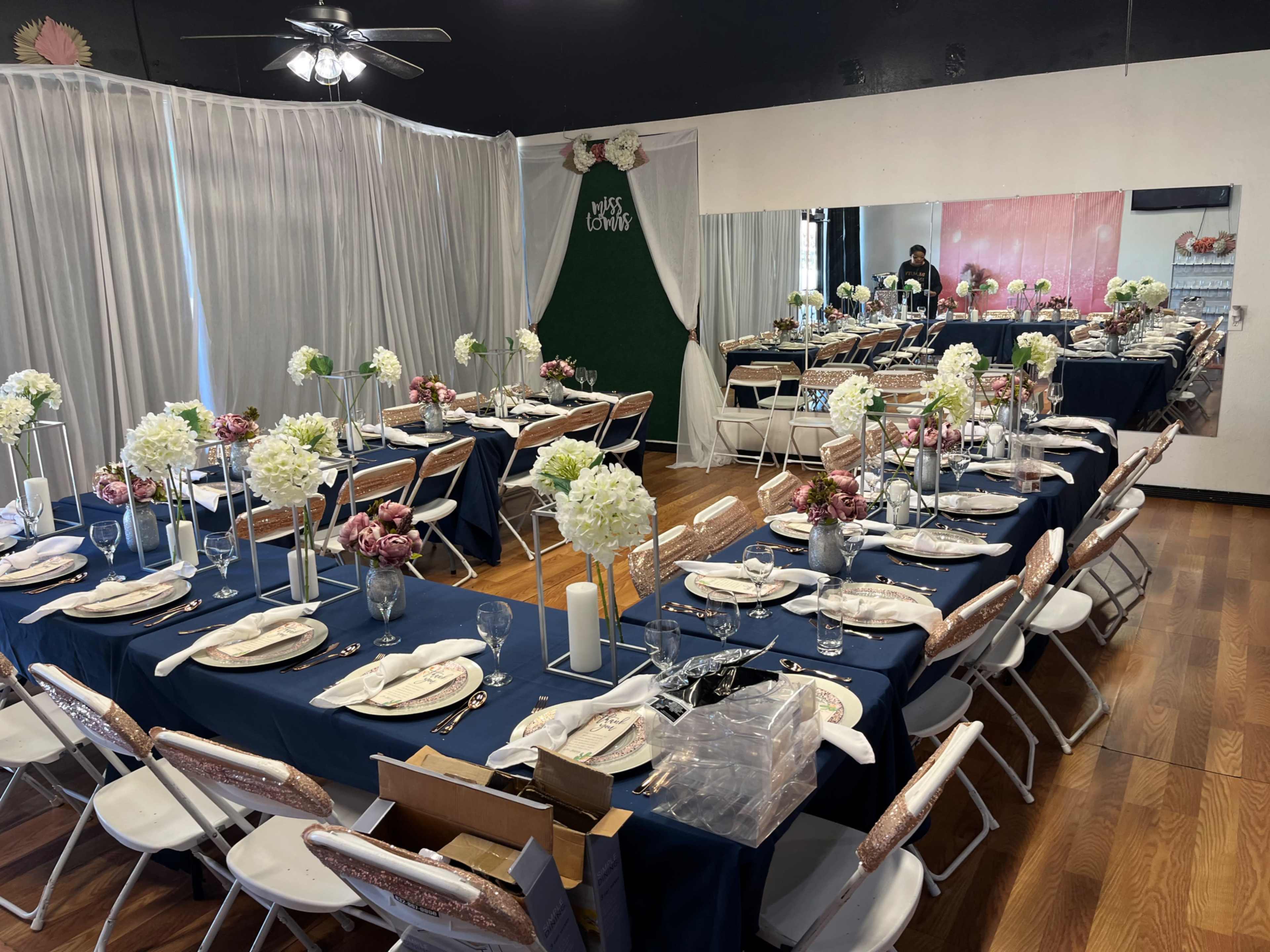 A banquet setup with tables covered in navy tablecloths, adorned with flower arrangements and place settings in a decorated room.