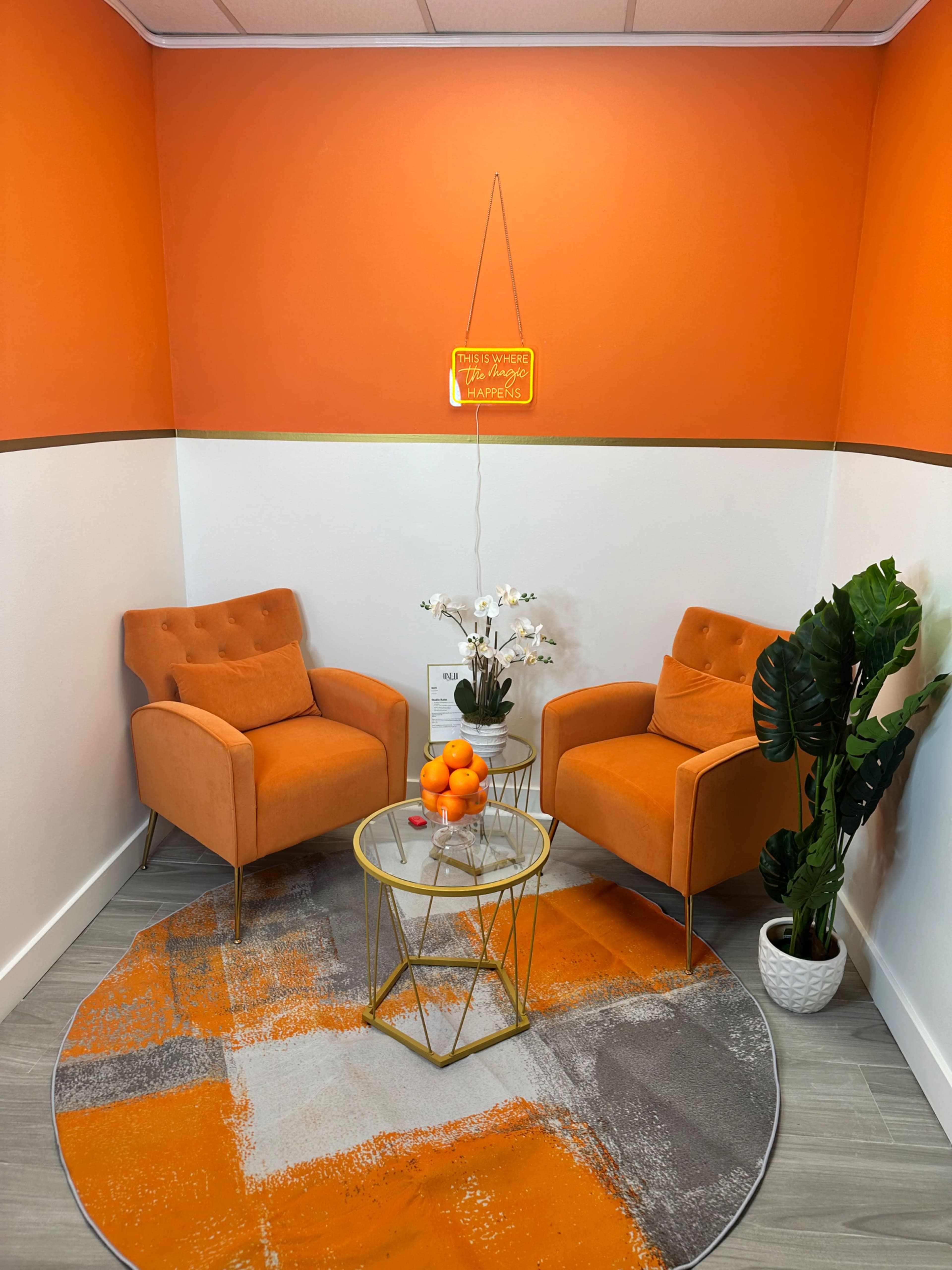 A small room with orange walls, two orange armchairs, a round coffee table with oranges, and a potted plant.