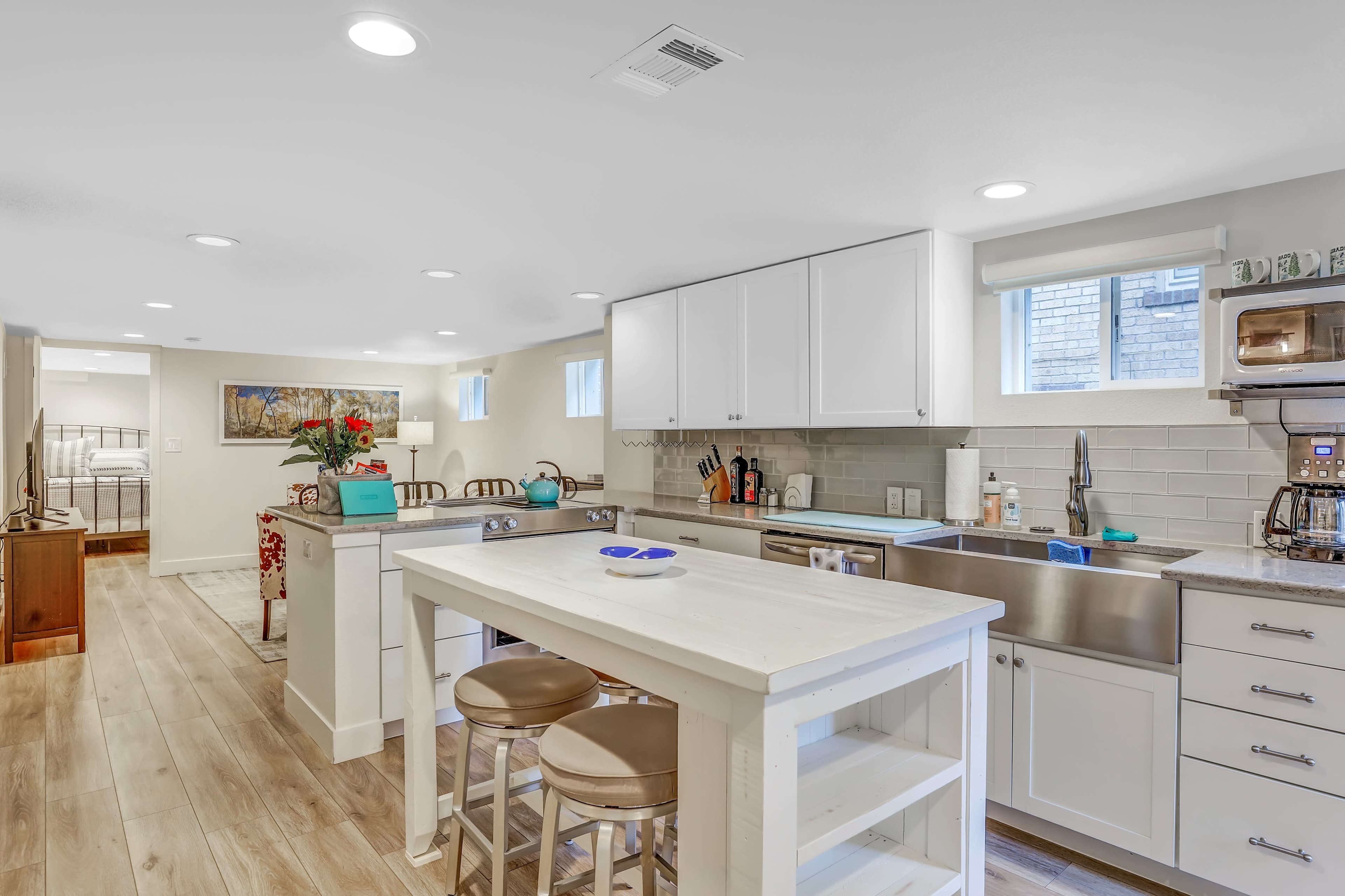 The image shows a modern kitchen with white cabinetry, a large central island, stainless steel appliances, and a light-colored wood floor.