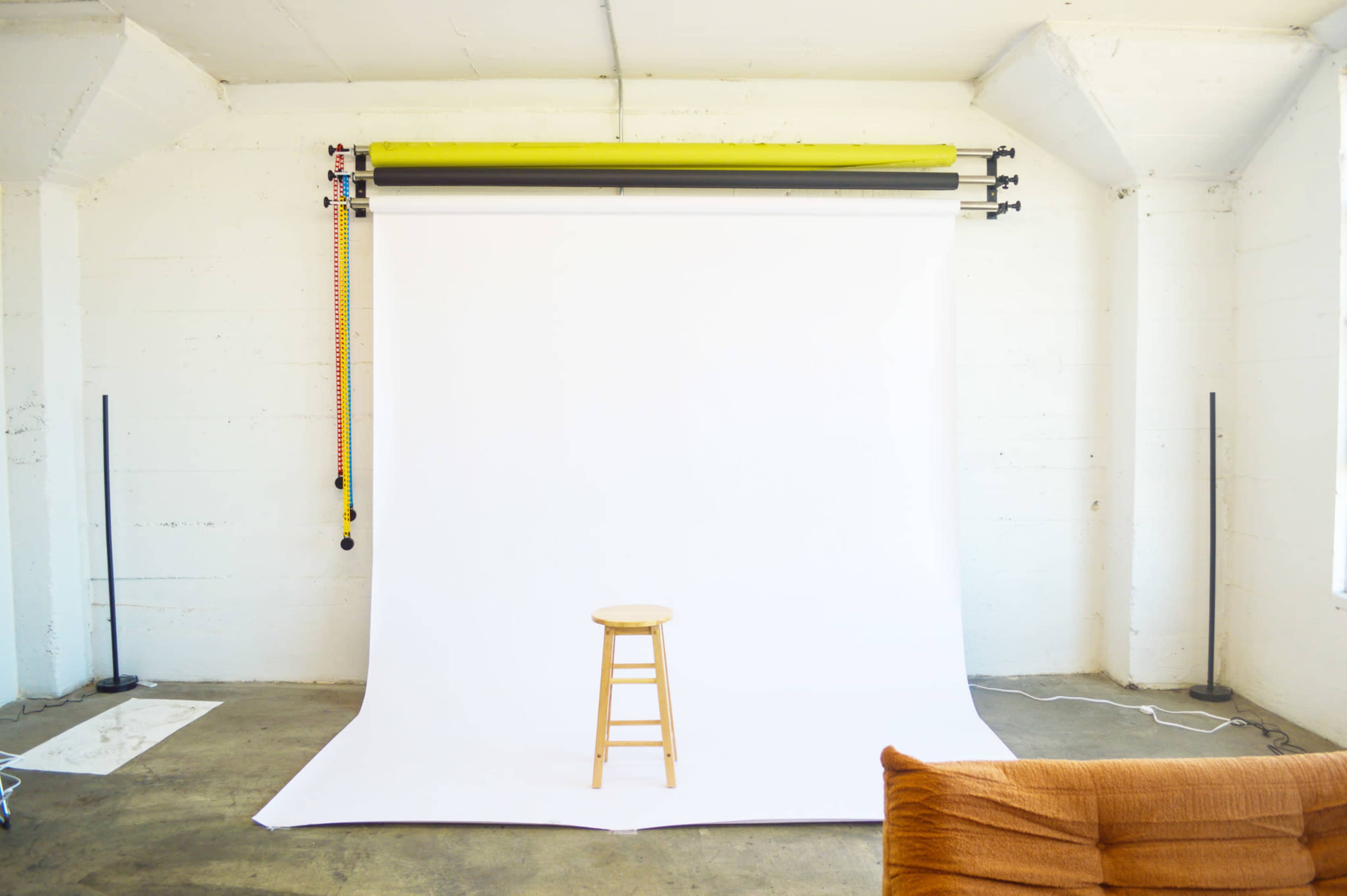 A bare room features a wooden stool in front of a white backdrop supported by a roller system.
