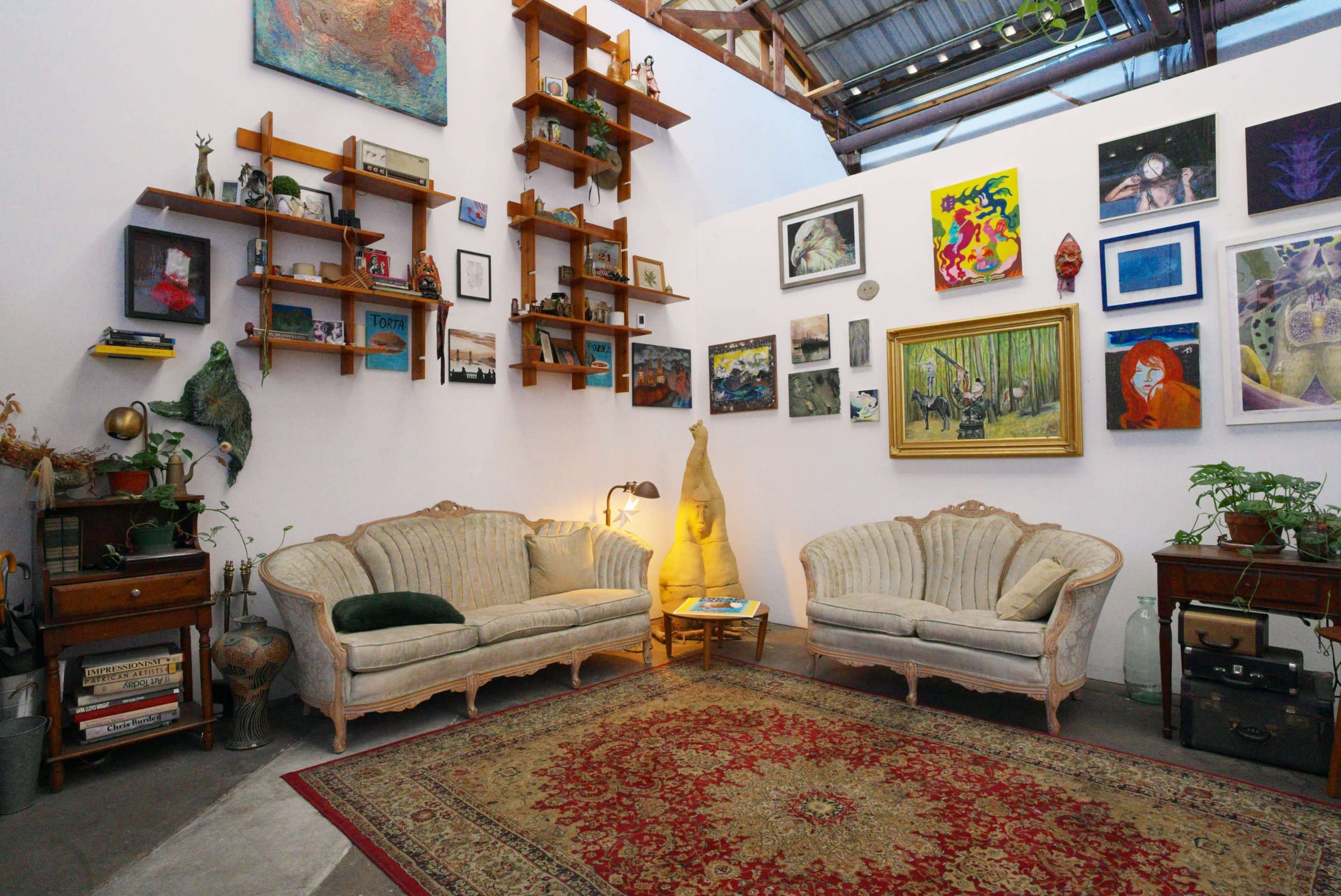 The image shows a cozy living area with two vintage sofas facing each other, surrounded by colorful wall art and shelves displaying various decorative items.