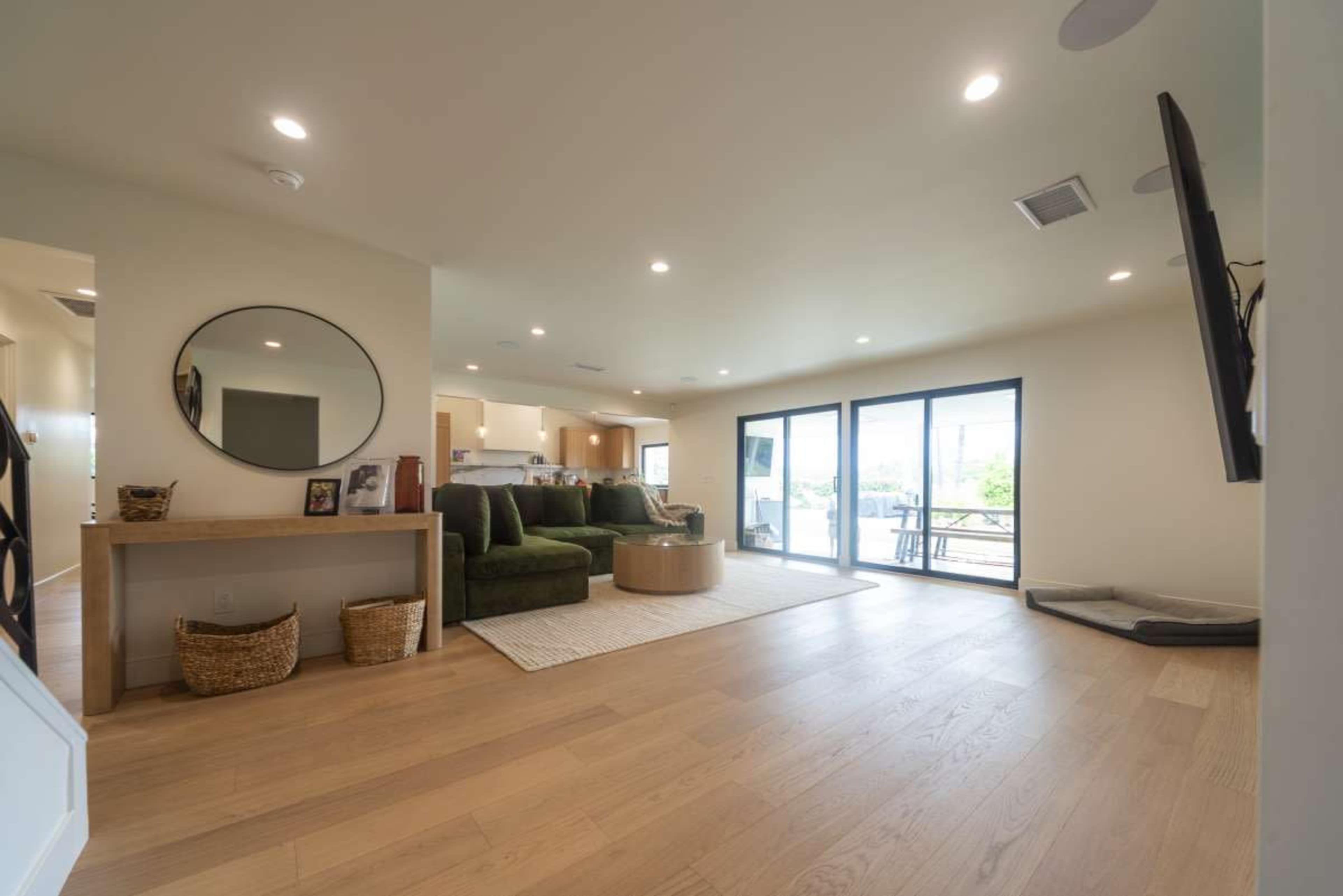 A bright living room features green sofas, a mirror, and large sliding glass doors leading to an outdoor area.
