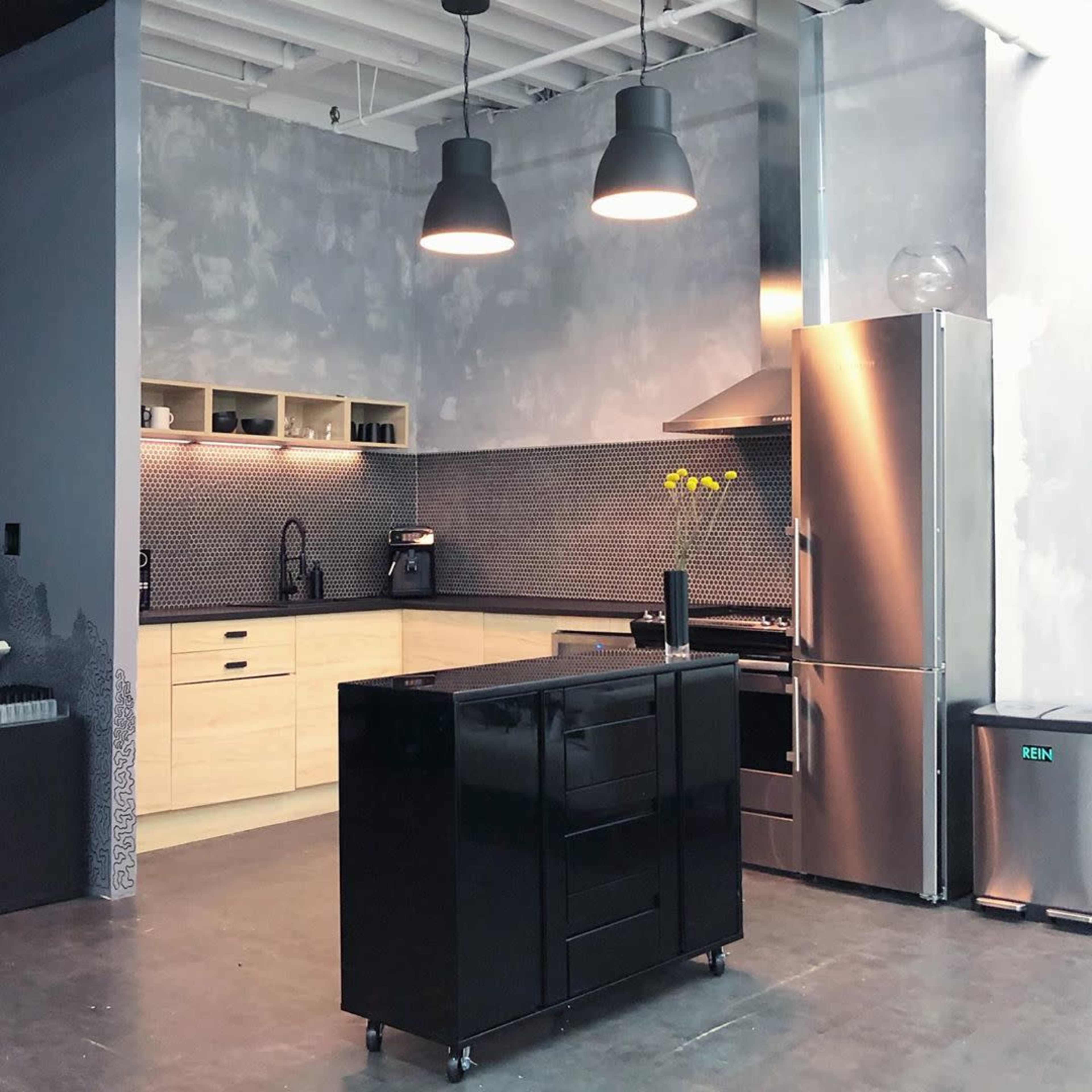 The kitchen features a black island, stainless steel appliances, and light wood cabinetry against a textured gray wall.