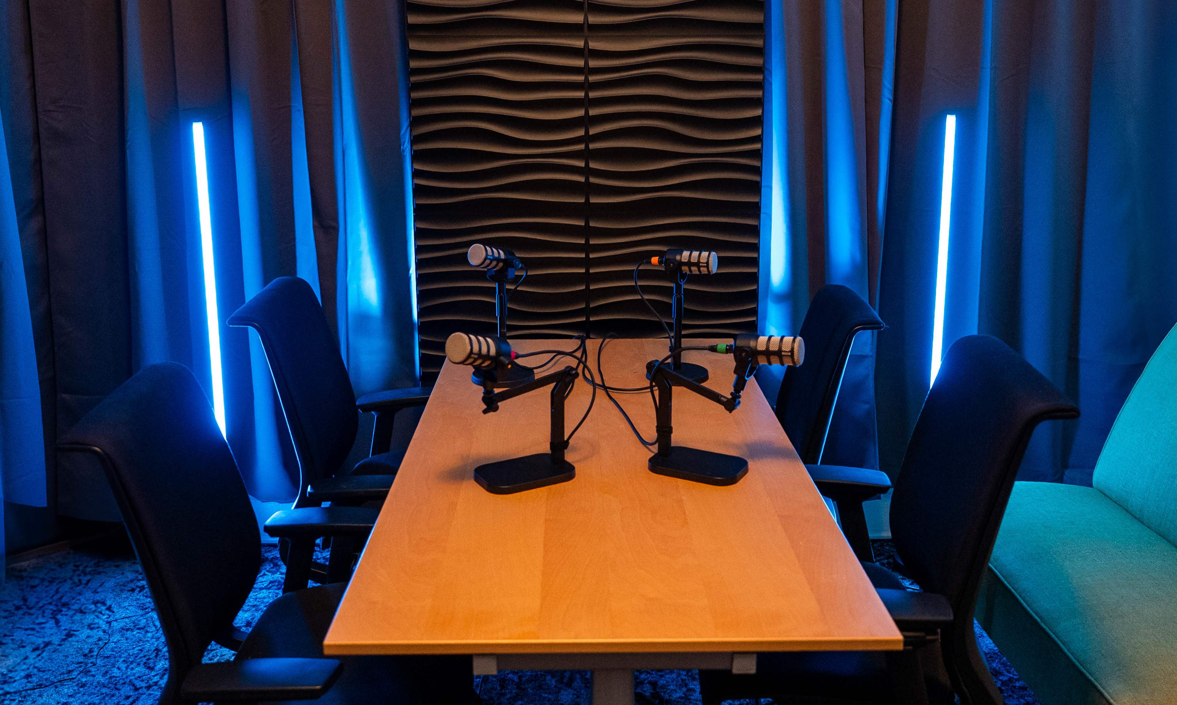 The image shows a meeting room with a wooden table, two microphones on stands, and blue lights illuminating the background.