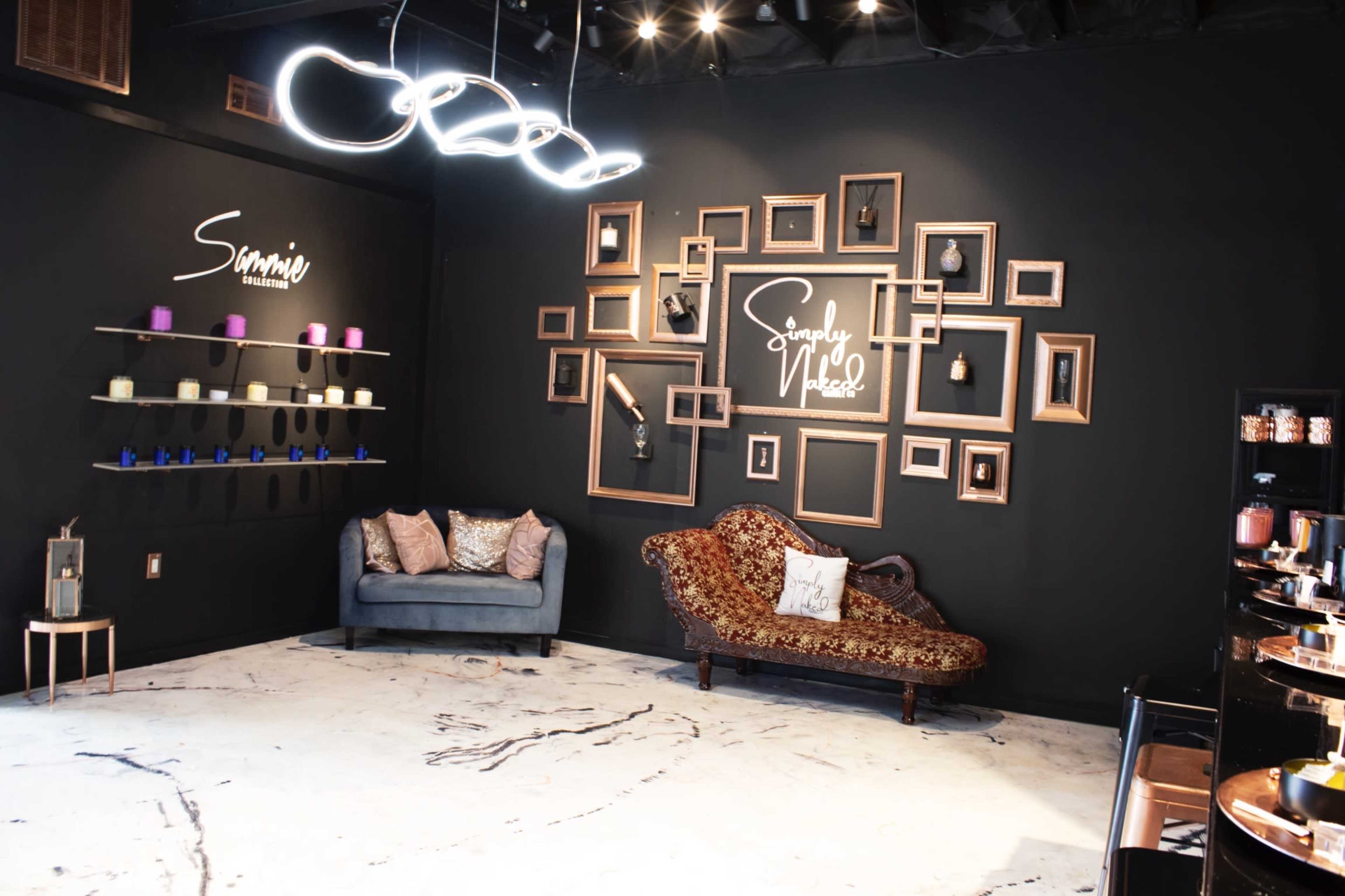 A modern interior space with black walls, featuring a seating area with a couch, a gallery wall of framed pictures, and decorative shelves with candles.