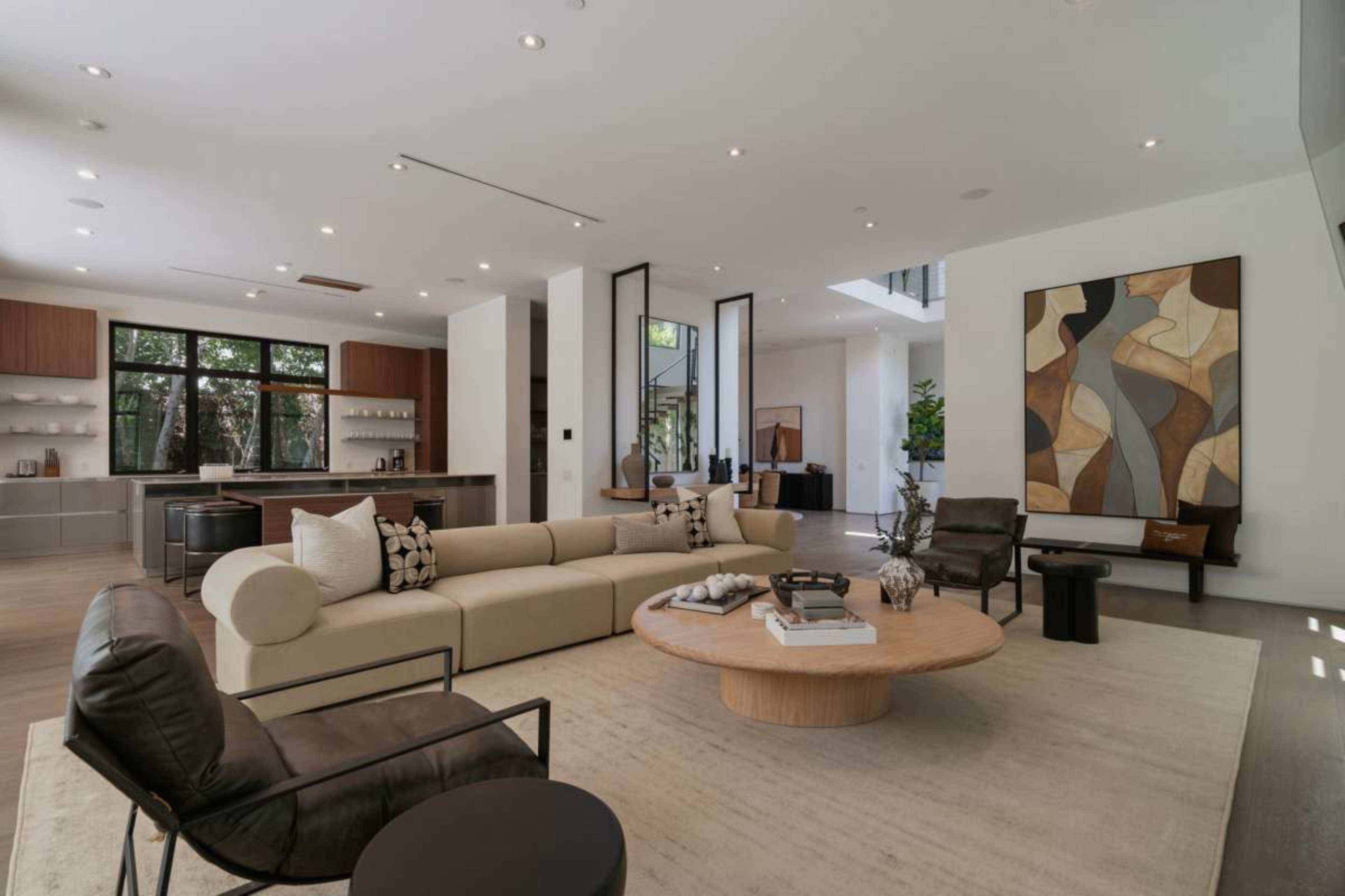 The image depicts a modern living room featuring a round coffee table, a sectional sofa, and large windows that allow natural light to enter the space.