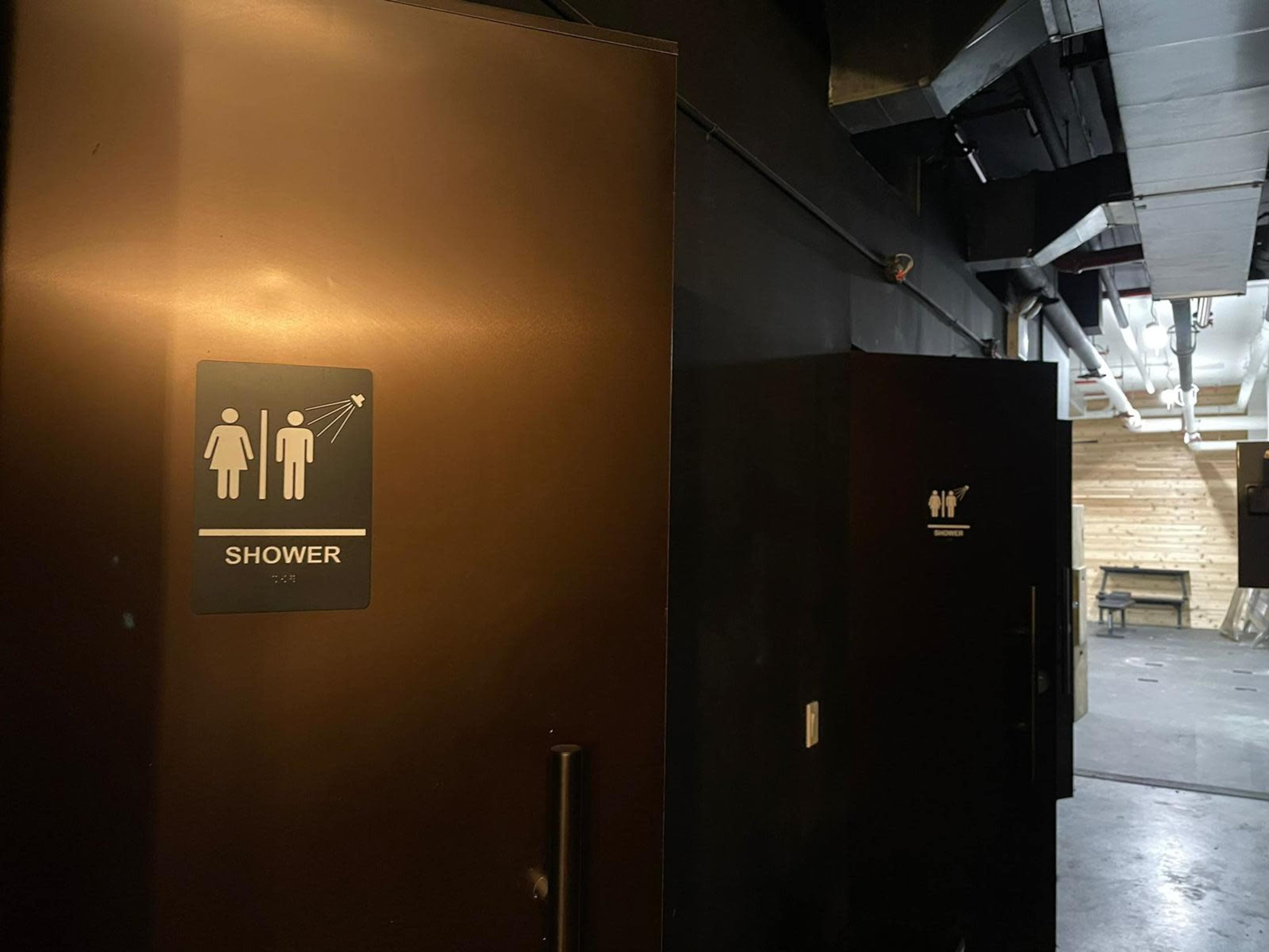 The image shows two doors in a dimly lit hallway, one labeled "SHOWER" with male and female symbols, and the other door is marked with privacy symbols.