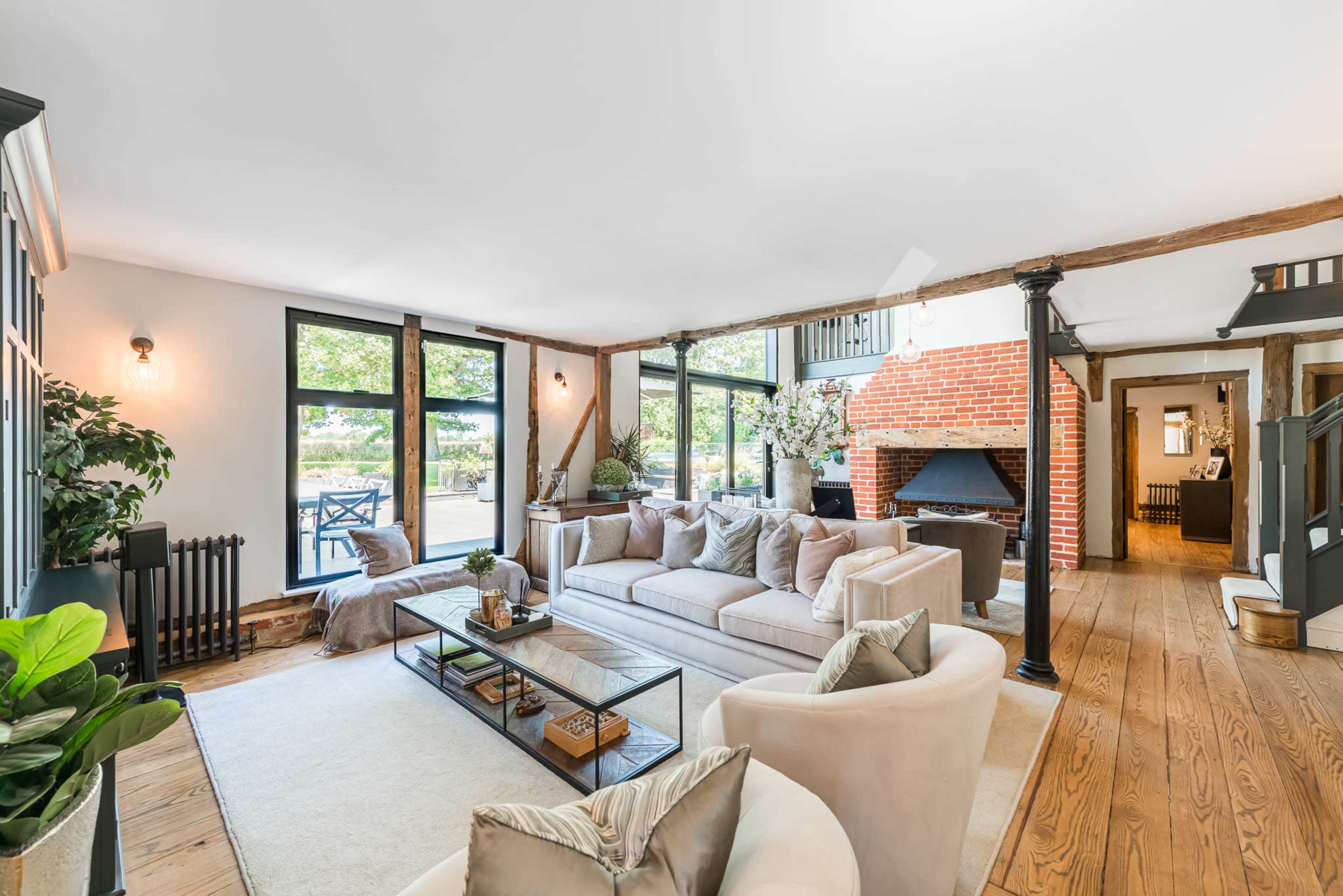 A spacious living room features a large sectional sofa, a coffee table, and a brick fireplace, with large windows overlooking a patio.