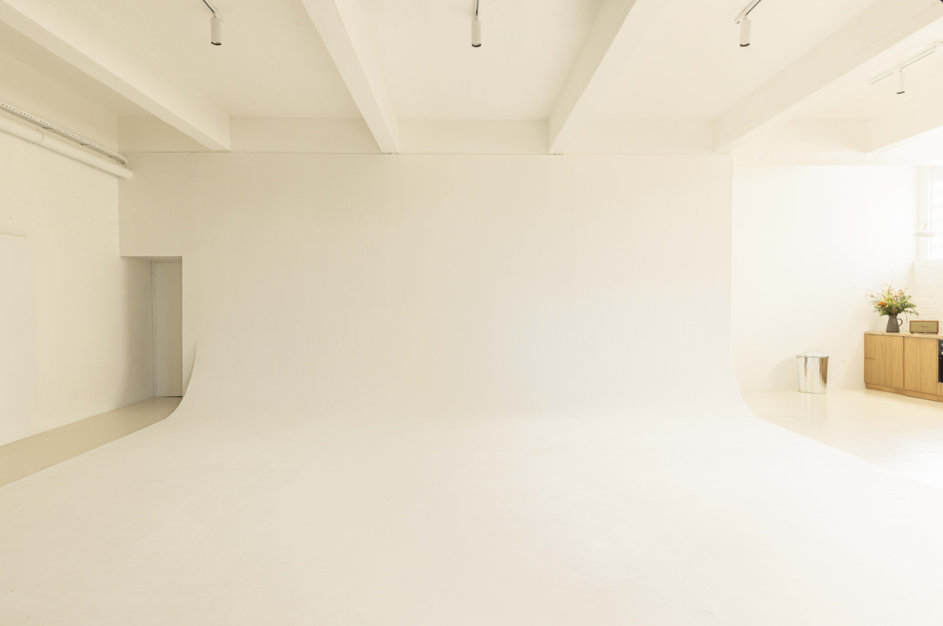 A minimalist photography studio with a large white backdrop and light-colored flooring.