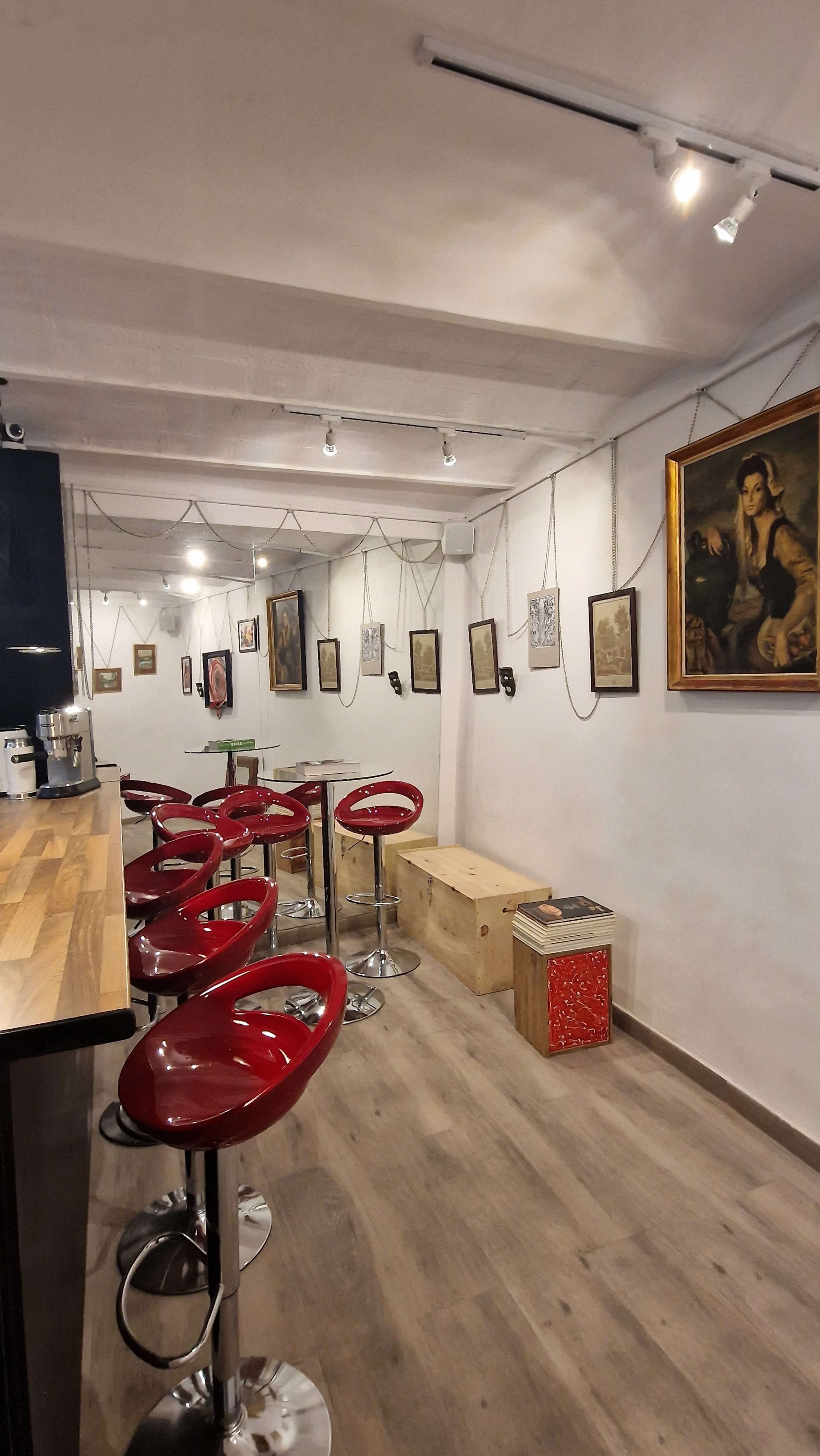 A minimalist cafe features red bar stools arranged at a wooden counter, with framed artwork displayed on the walls.