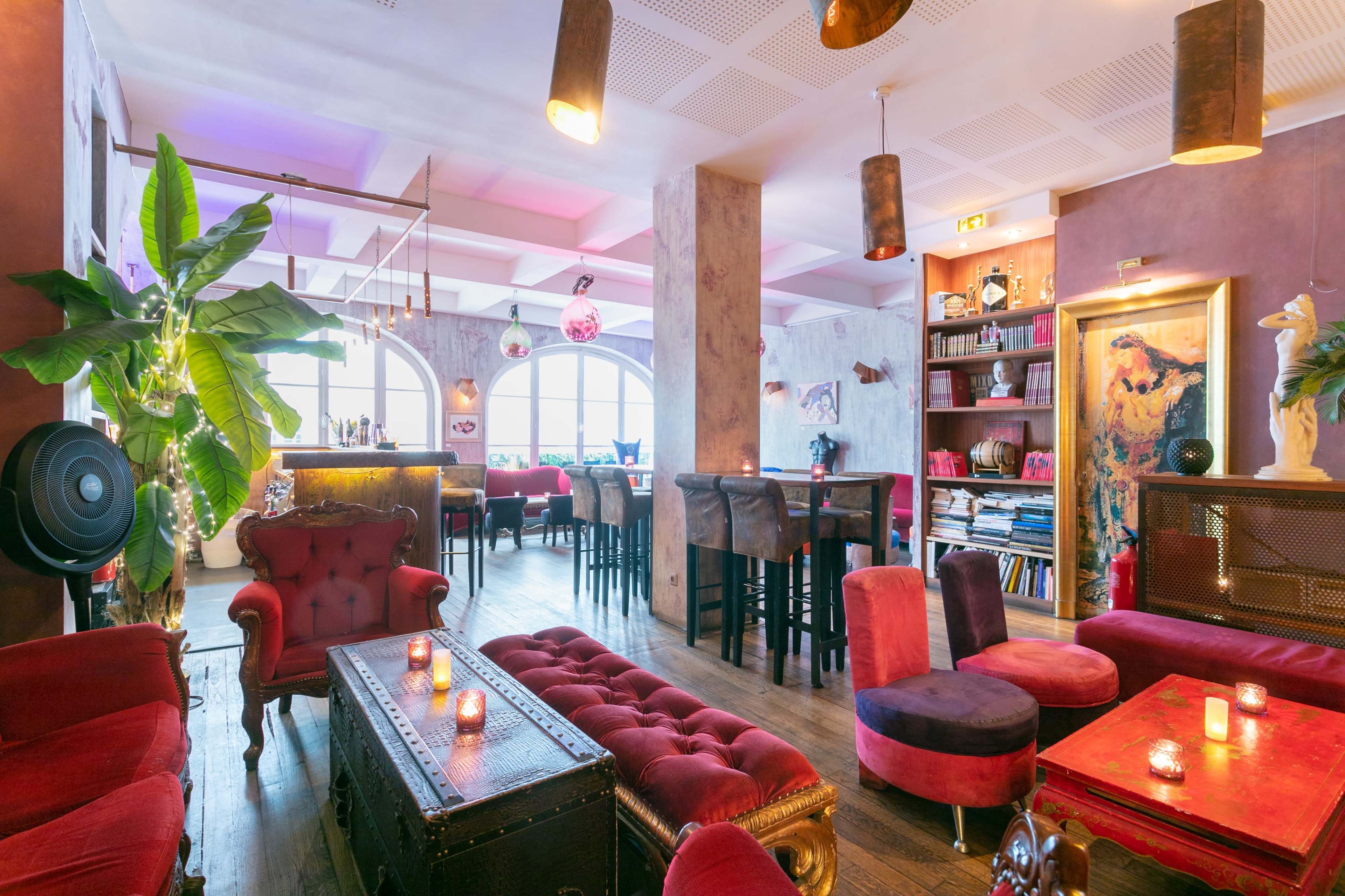 A colorful bar interior with vintage seating, a variety of plants, and dim lighting, creating a cozy atmosphere.