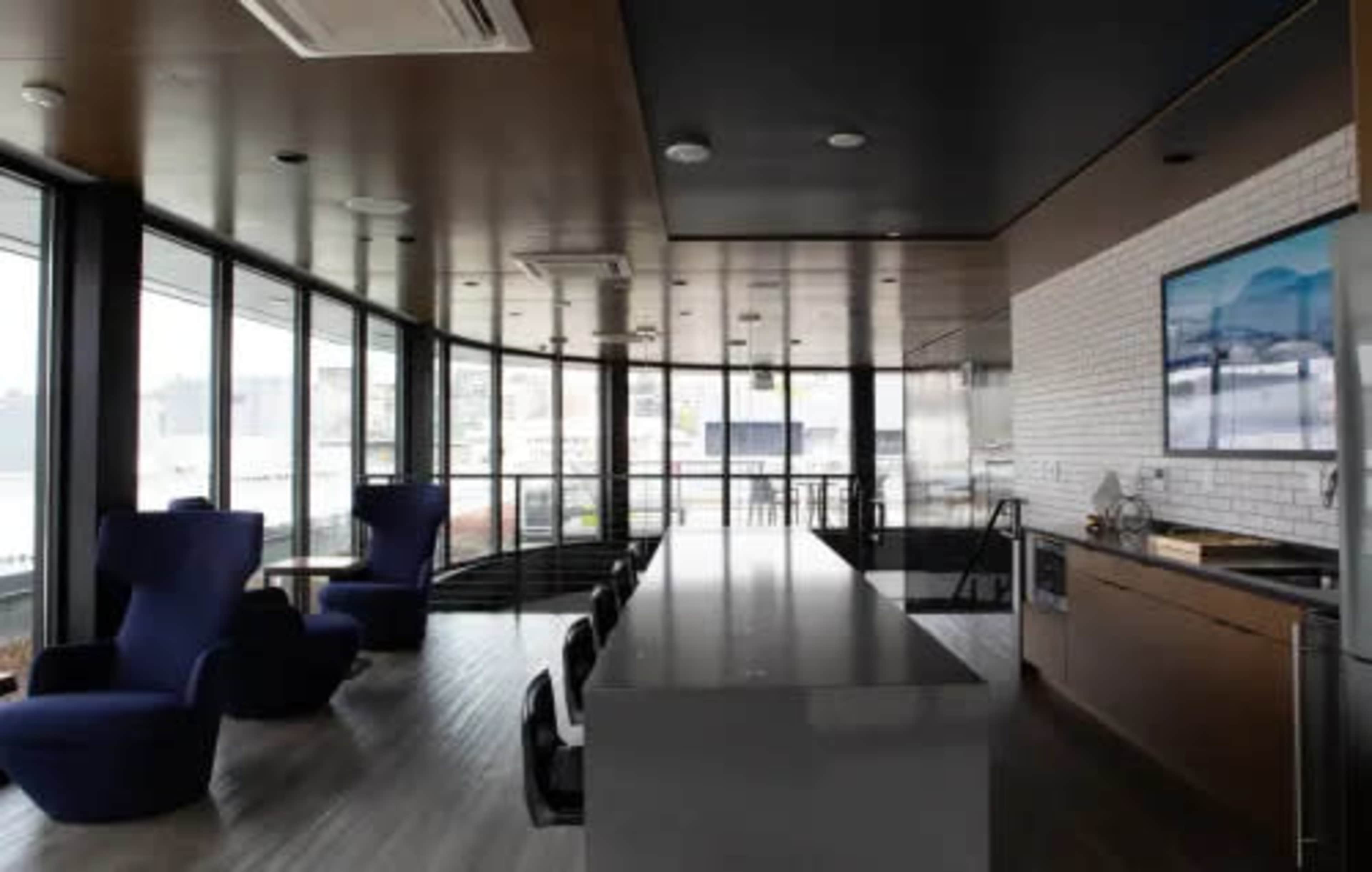 A modern kitchen with large windows, a long gray island, and dark blue seating areas.