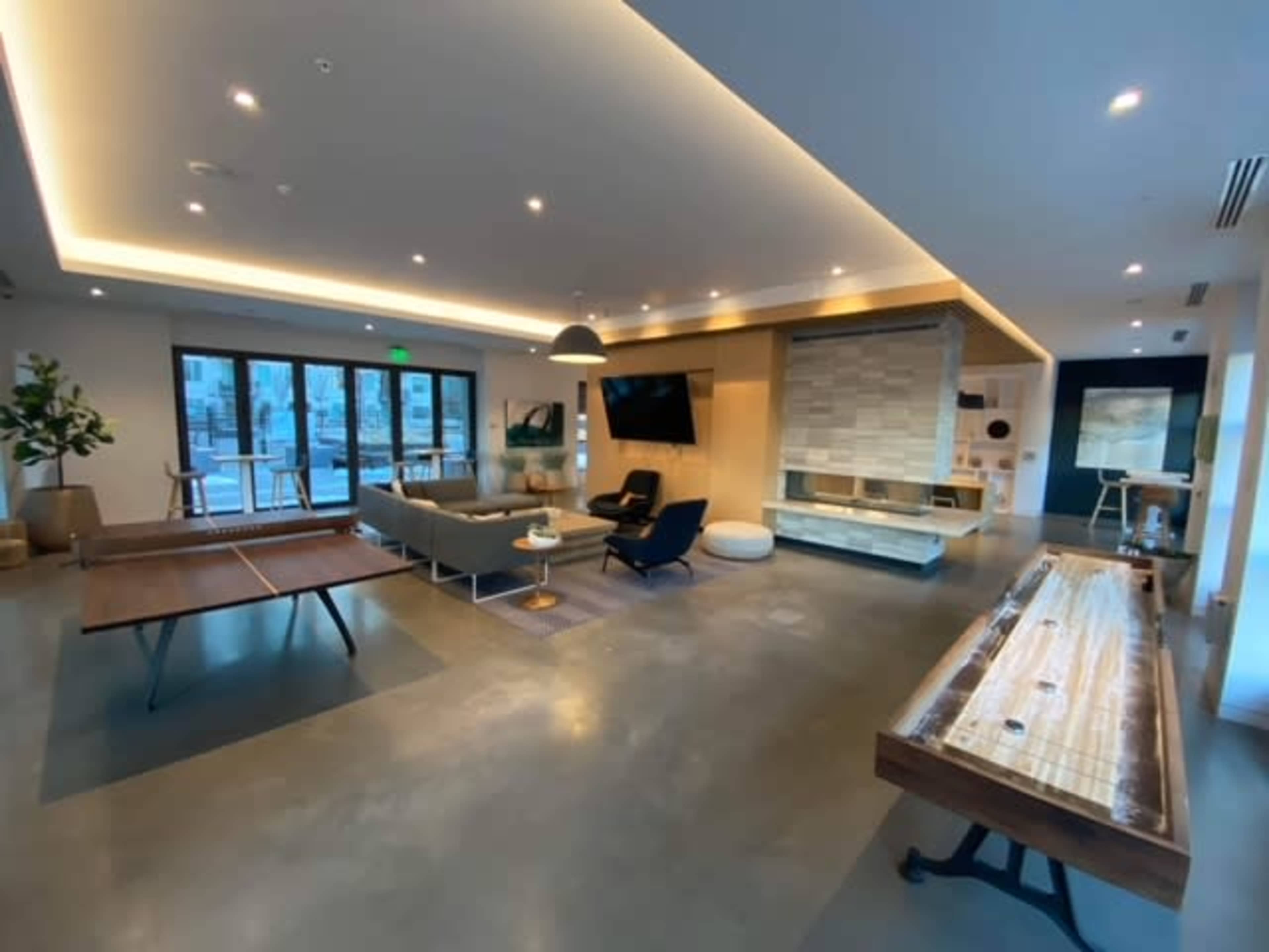 A modern lounge area featuring a coffee table, seating, a television, and a fireplace, with large windows allowing natural light.