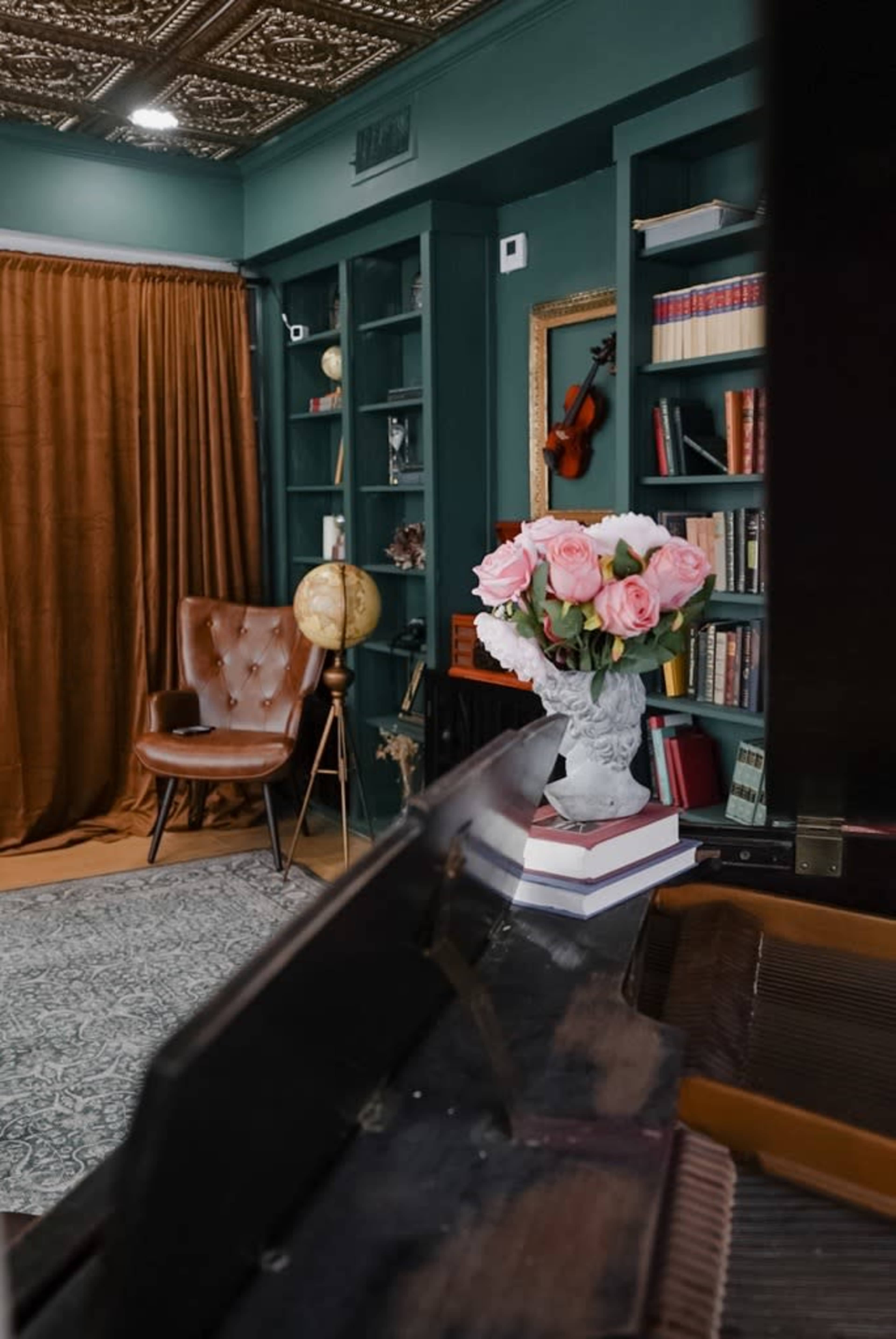 The image showcases a cozy reading nook featuring a chair, a globe, bookshelves, a bouquet of flowers, and a curtain, with a view from a piano perspective.
