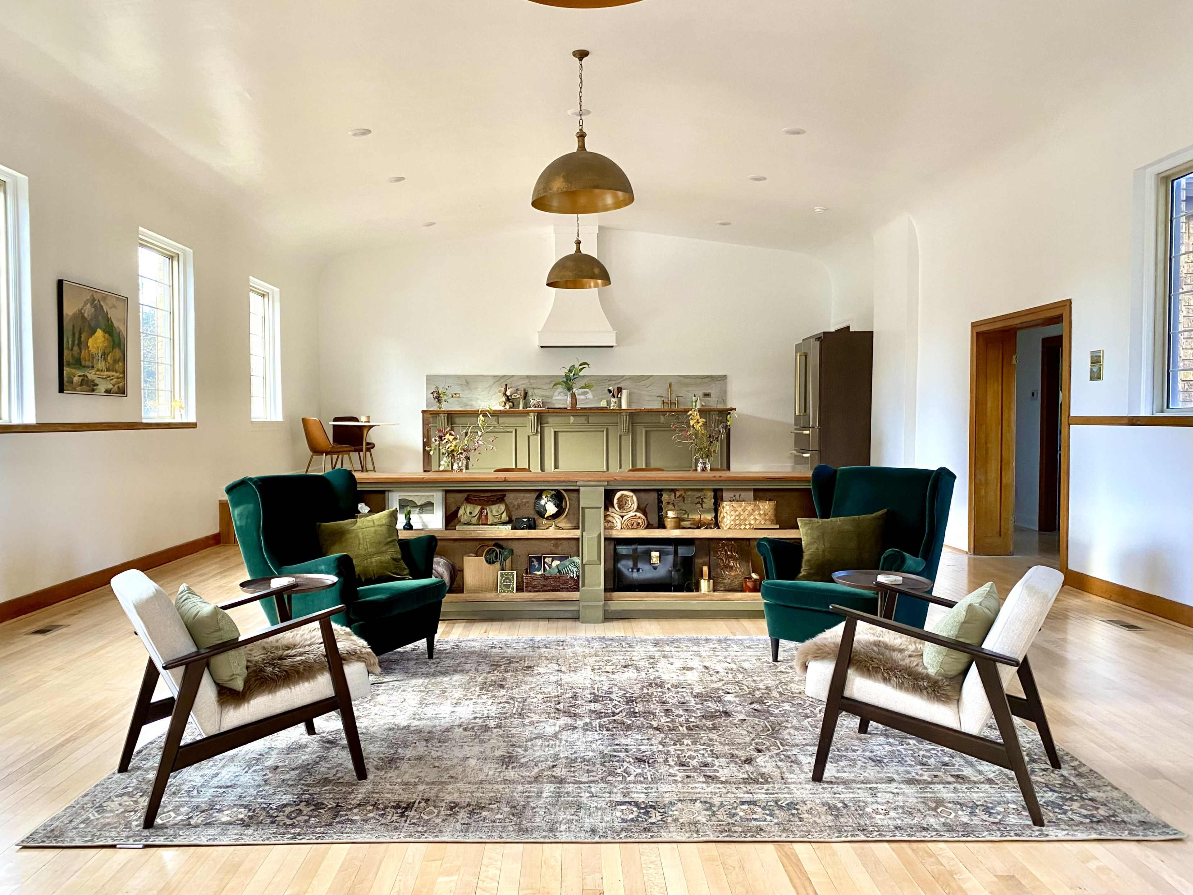 A spacious living room with two green armchairs and a light rug, centered around a wooden display unit against a white wall.