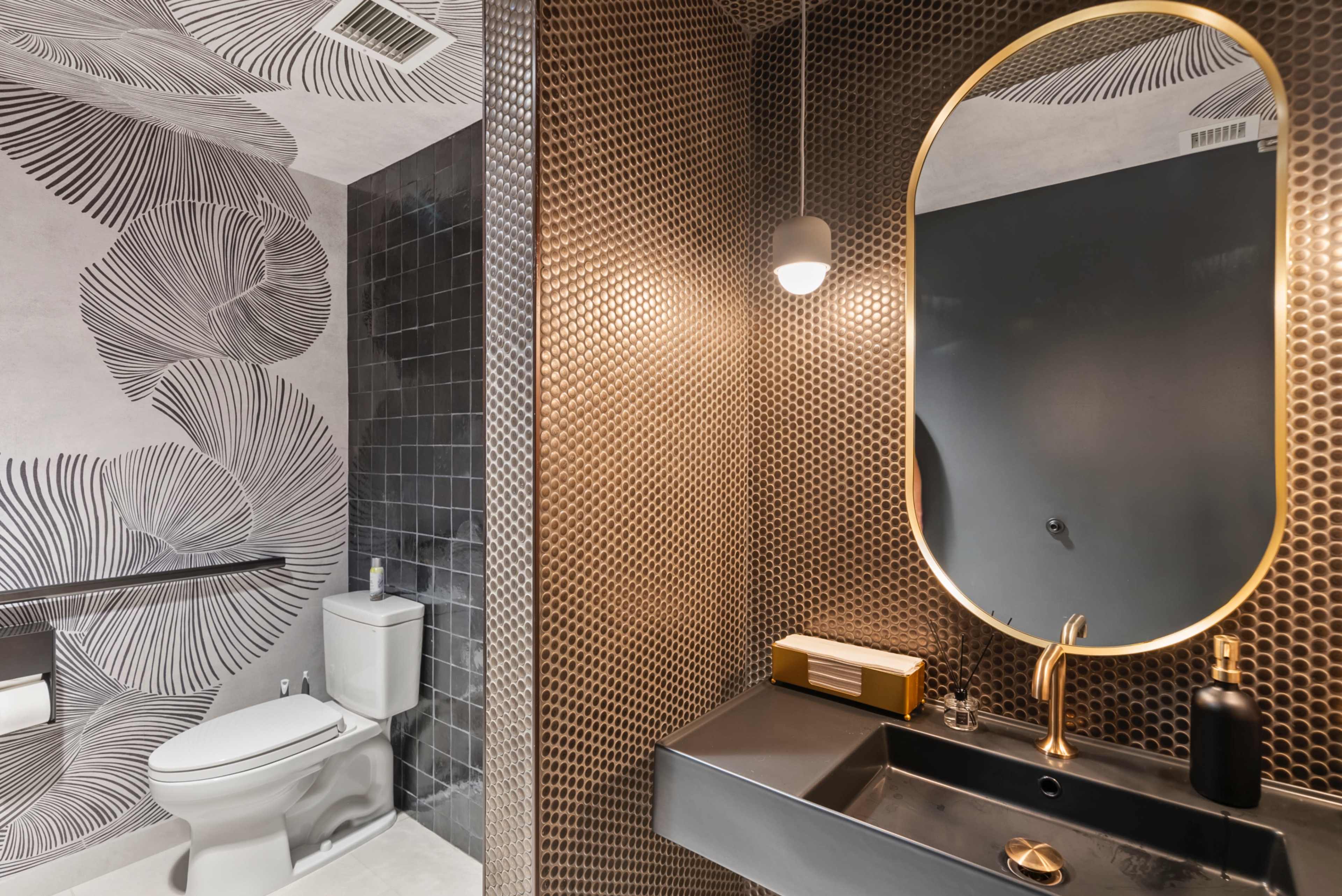 The image features a modern bathroom with a patterned wallpaper, a sleek black sink, a round mirror, and a white toilet.