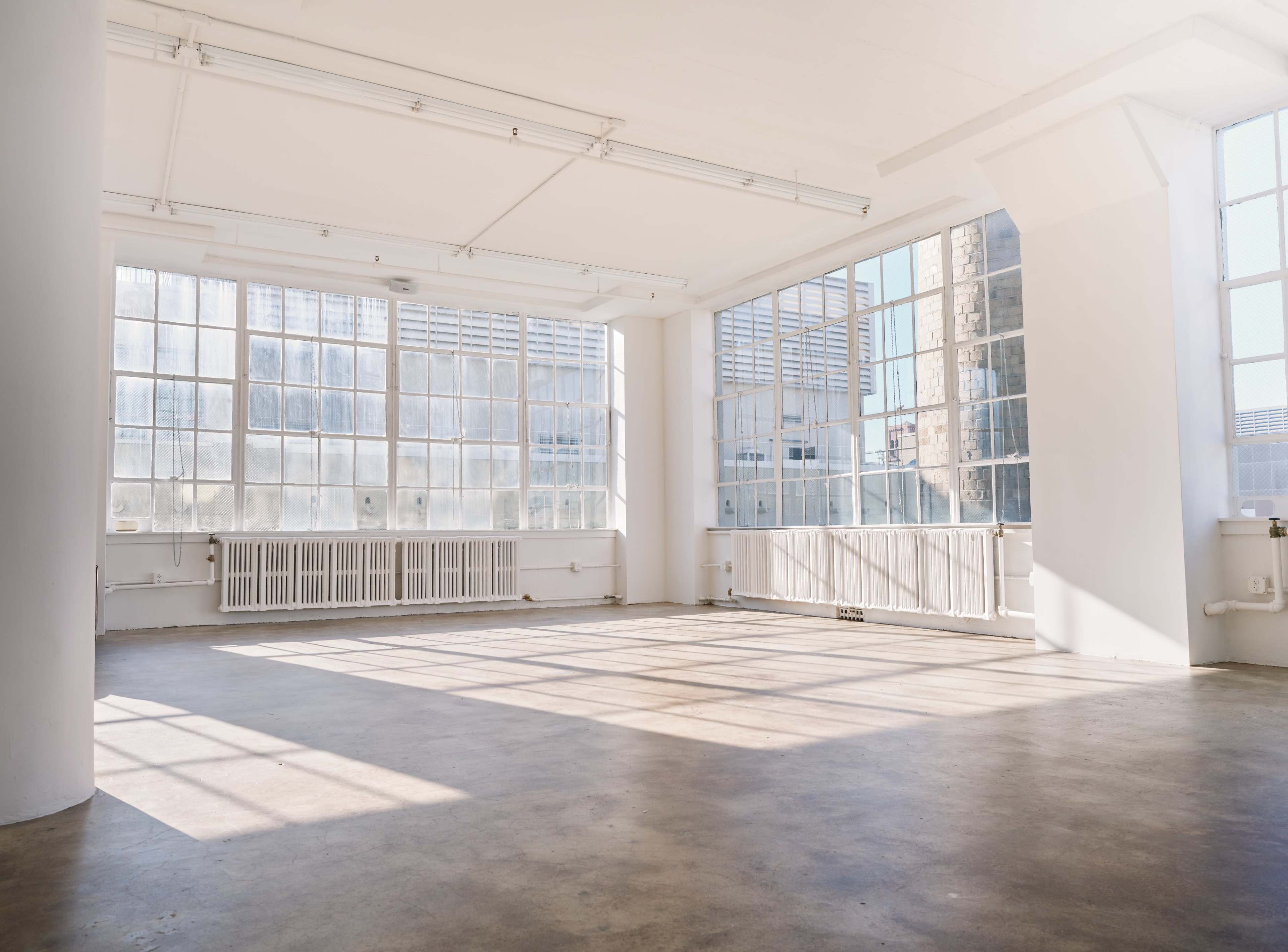 A spacious, sunlit room with large windows and a concrete floor.
