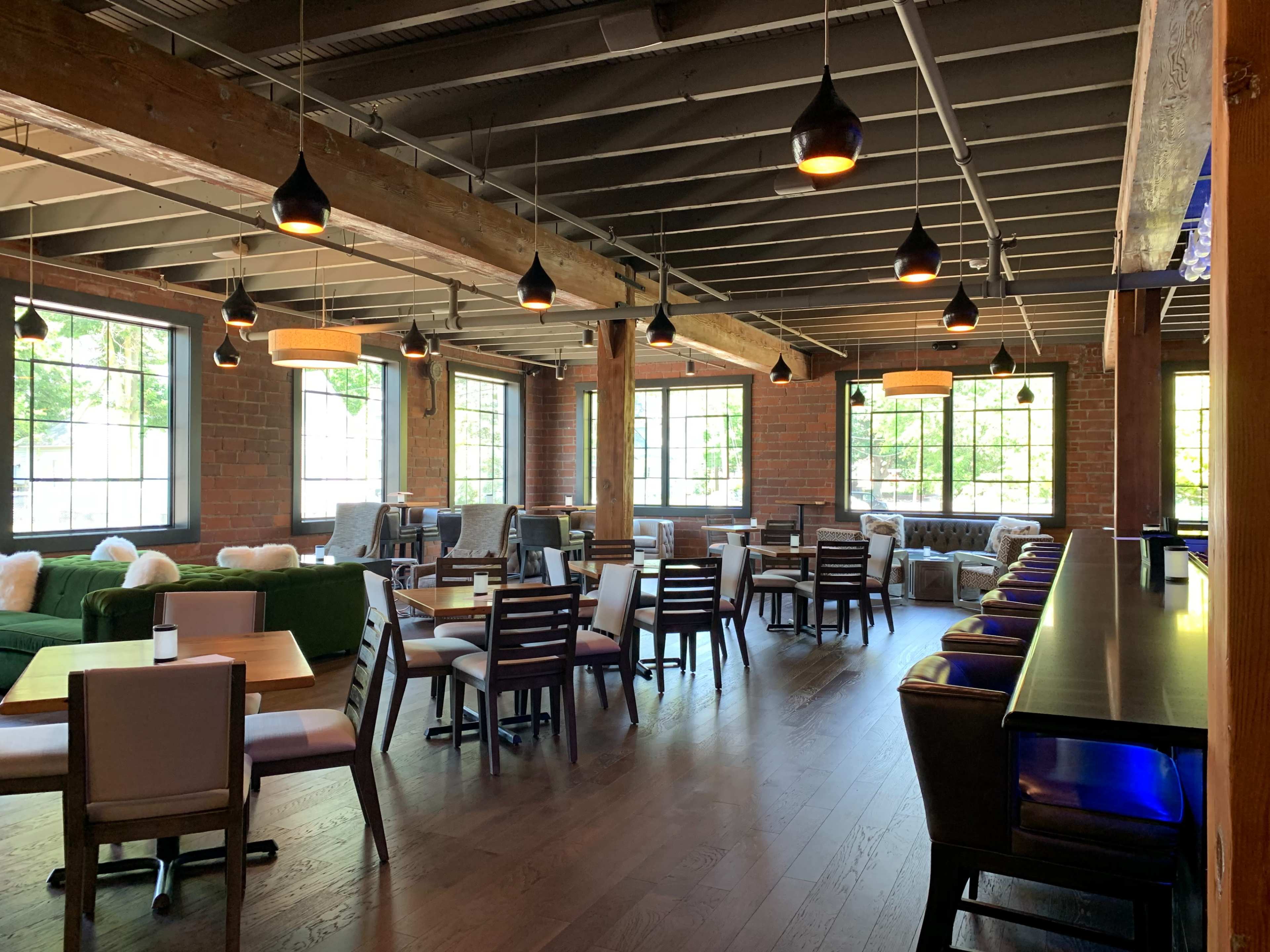 A spacious restaurant interior with wooden floors, several tables and chairs, and large windows letting in natural light.