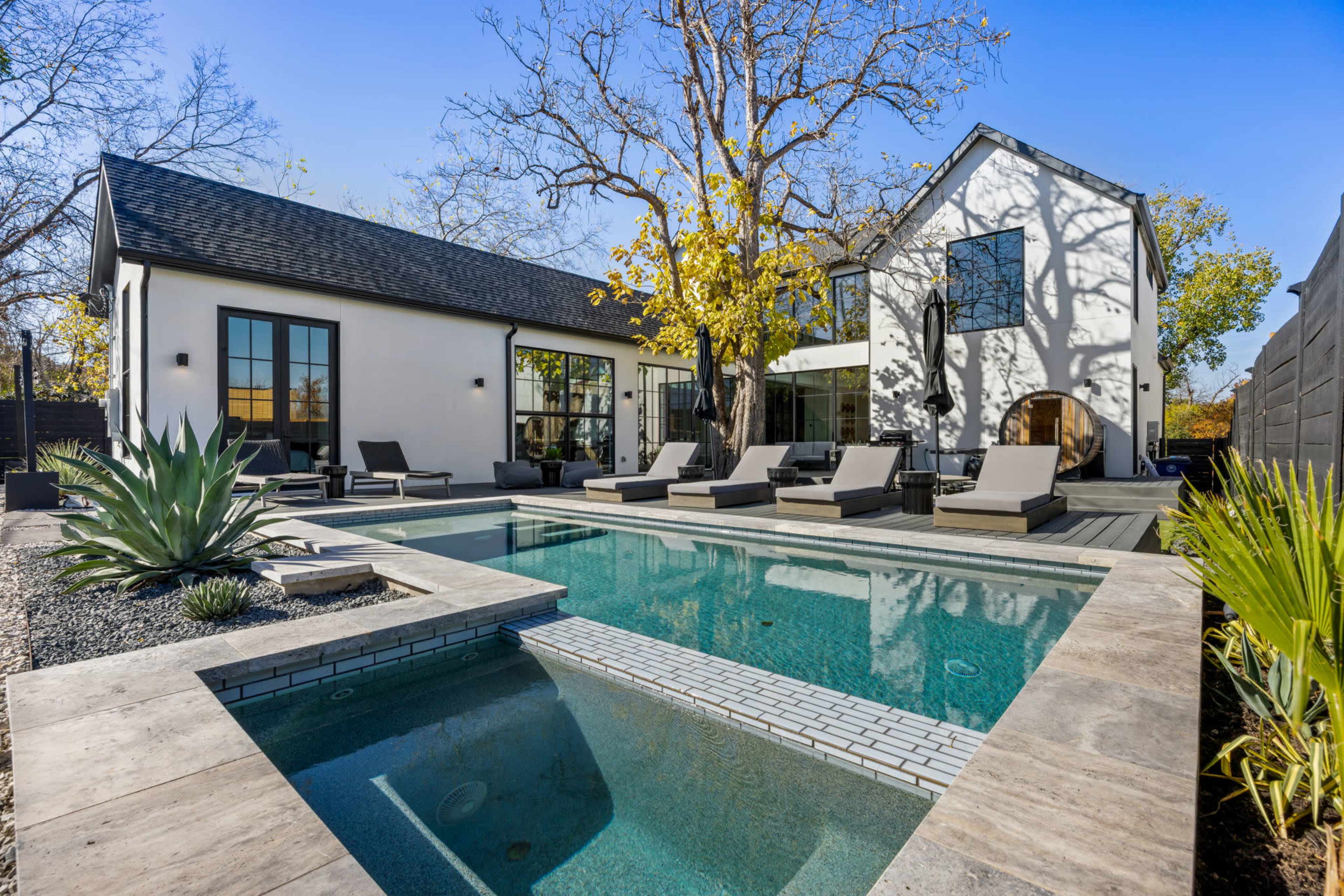 The image depicts a modern backyard featuring a rectangular swimming pool with lounge chairs, surrounded by landscaped areas and a two-story home with large windows.