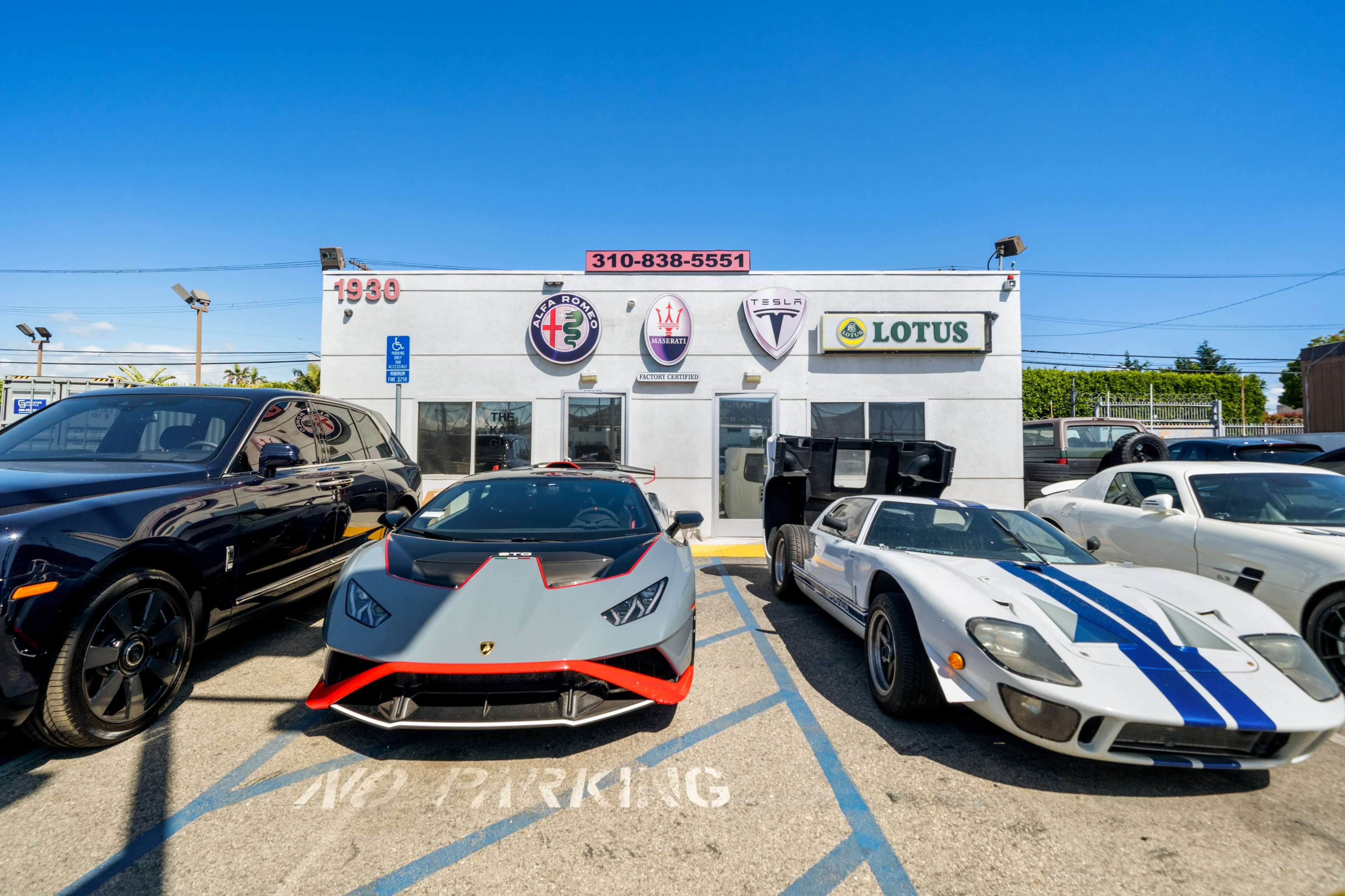 The image shows a row of luxury cars, including a Lamborghini and a Ford GT, parked in front of a building with several automotive brand logos.