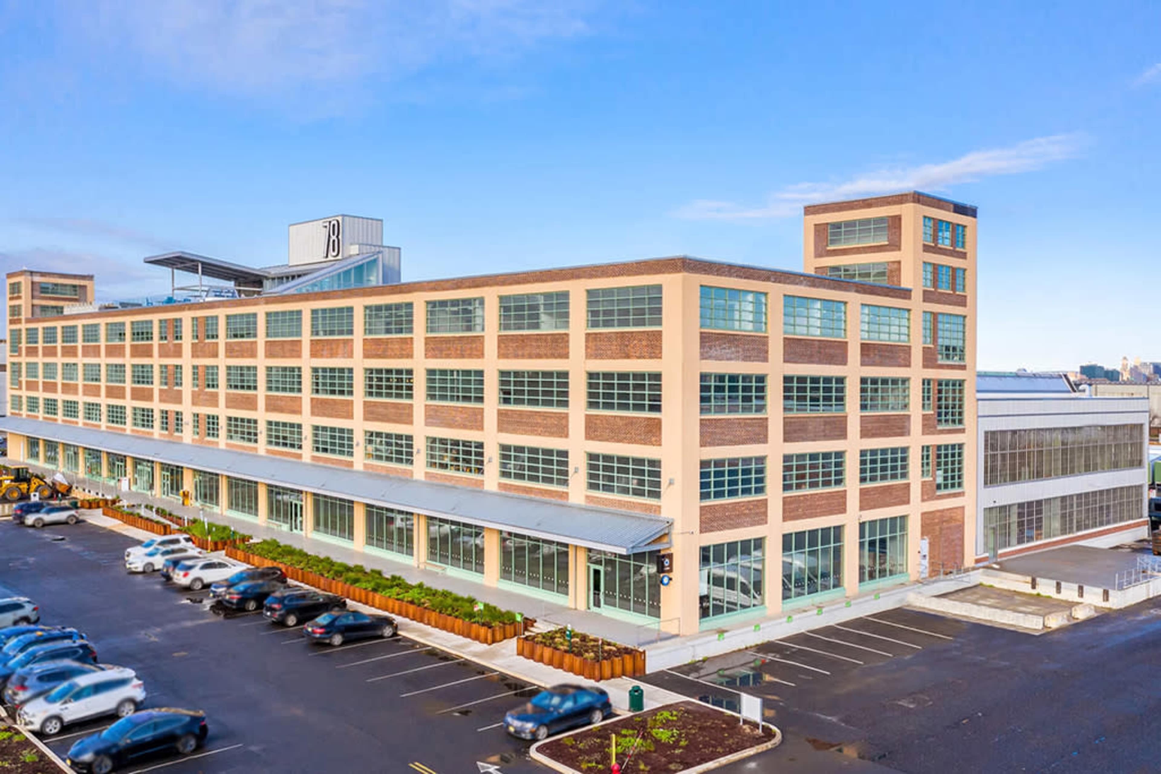 The image shows a large, multi-story brick building with numerous windows, surrounded by a parking lot filled with cars.