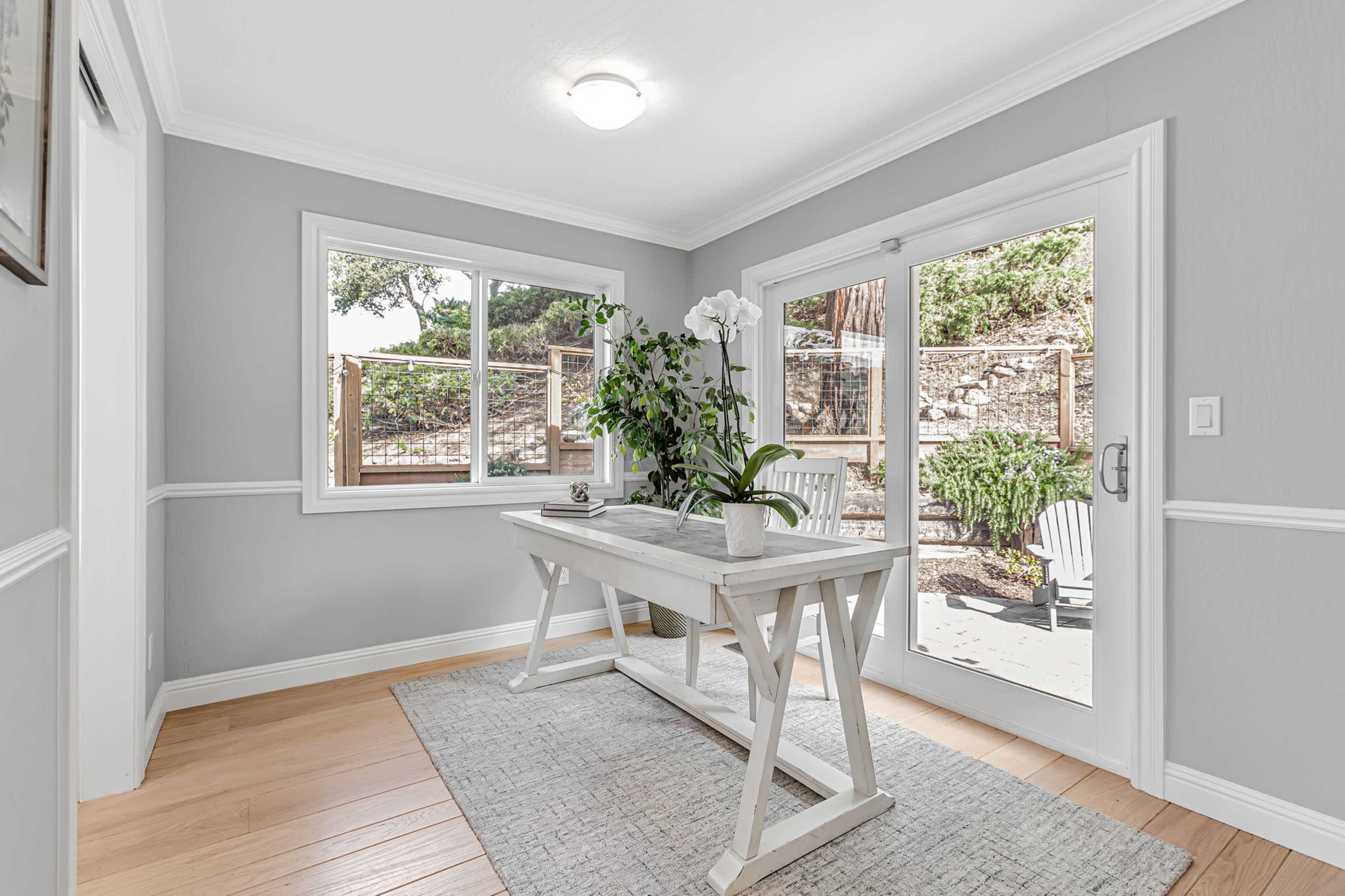A bright room features a white table with a potted plant, large windows, and a glass door leading to an outdoor area.