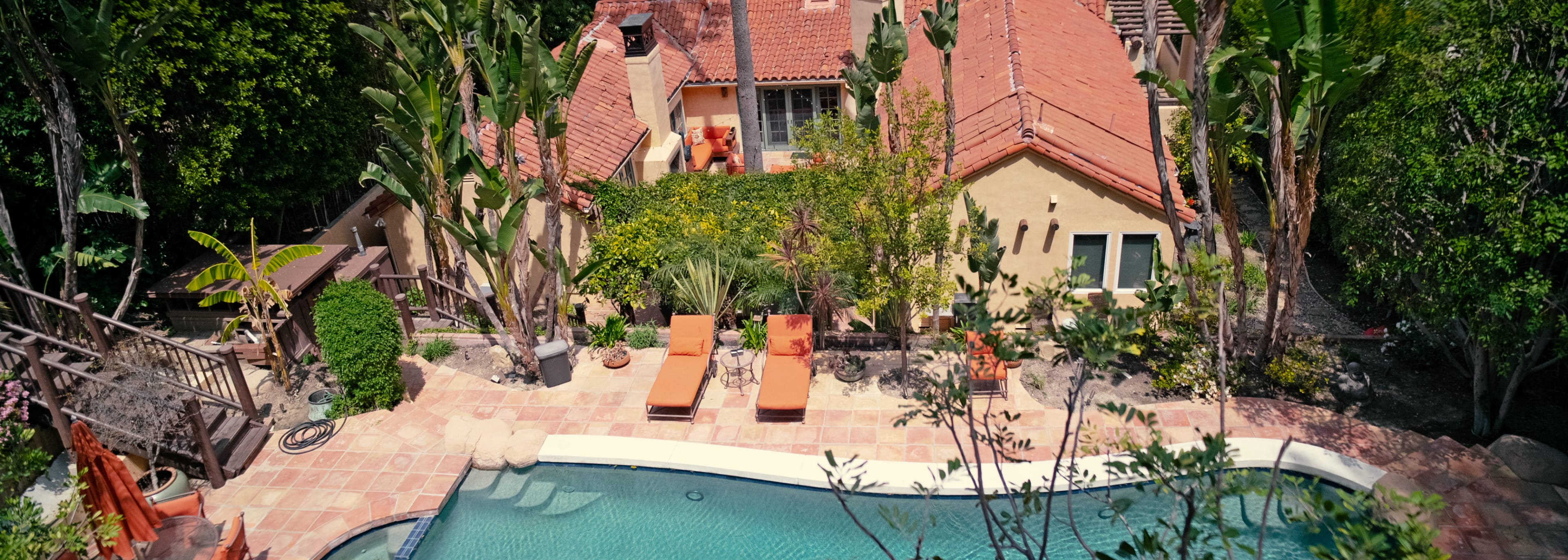 A landscaped backyard with a swimming pool and lounge chairs, adjacent to a house surrounded by greenery.