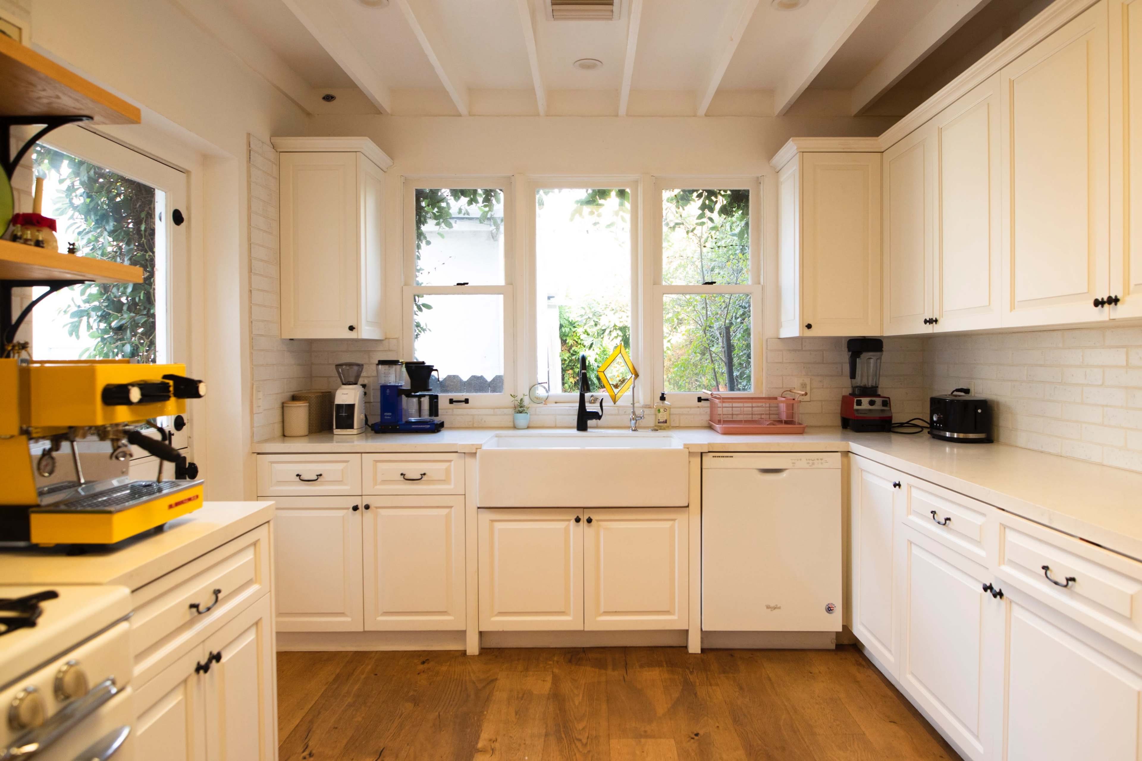 A bright kitchen featuring white cabinets, a farmhouse sink, and an arrangement of kitchen appliances along a counter.
