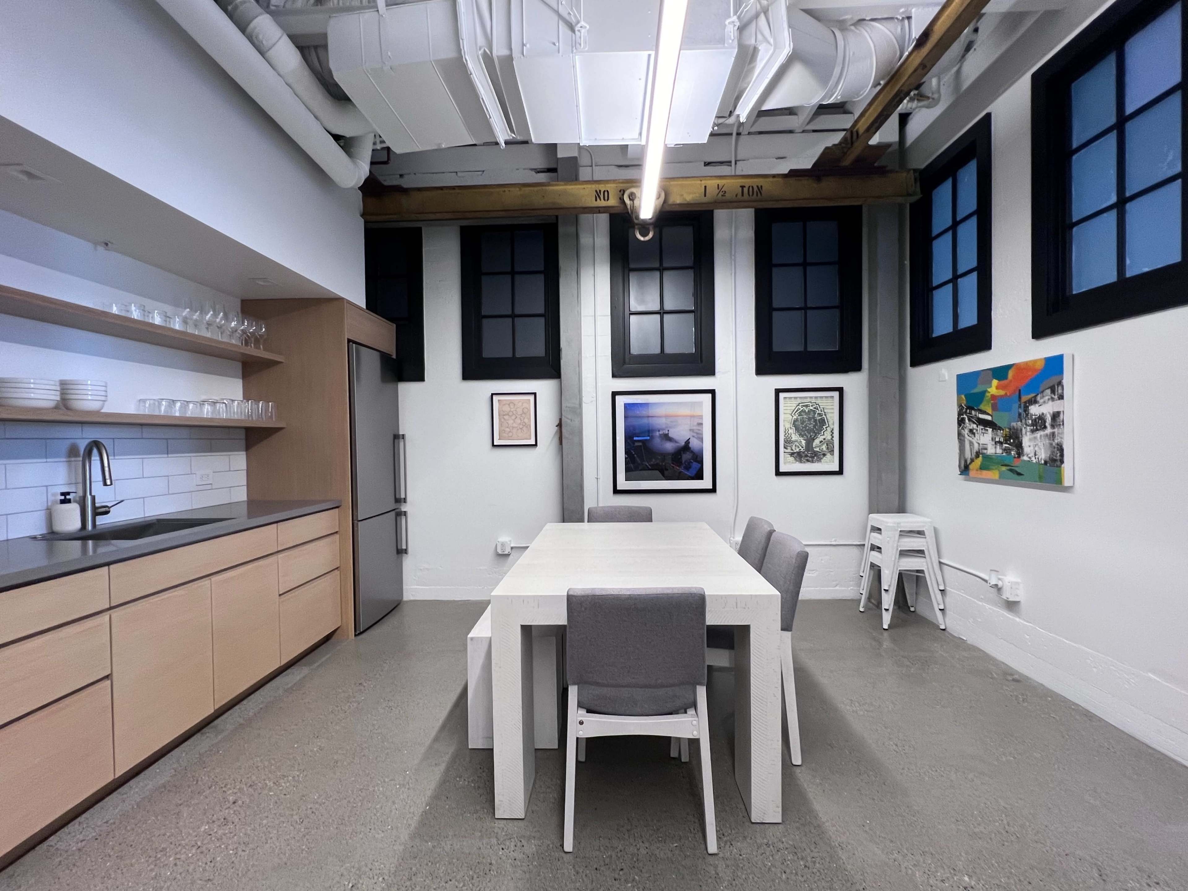 A modern kitchen with a large white table surrounded by gray chairs, cabinets with plates, and artwork on the walls.