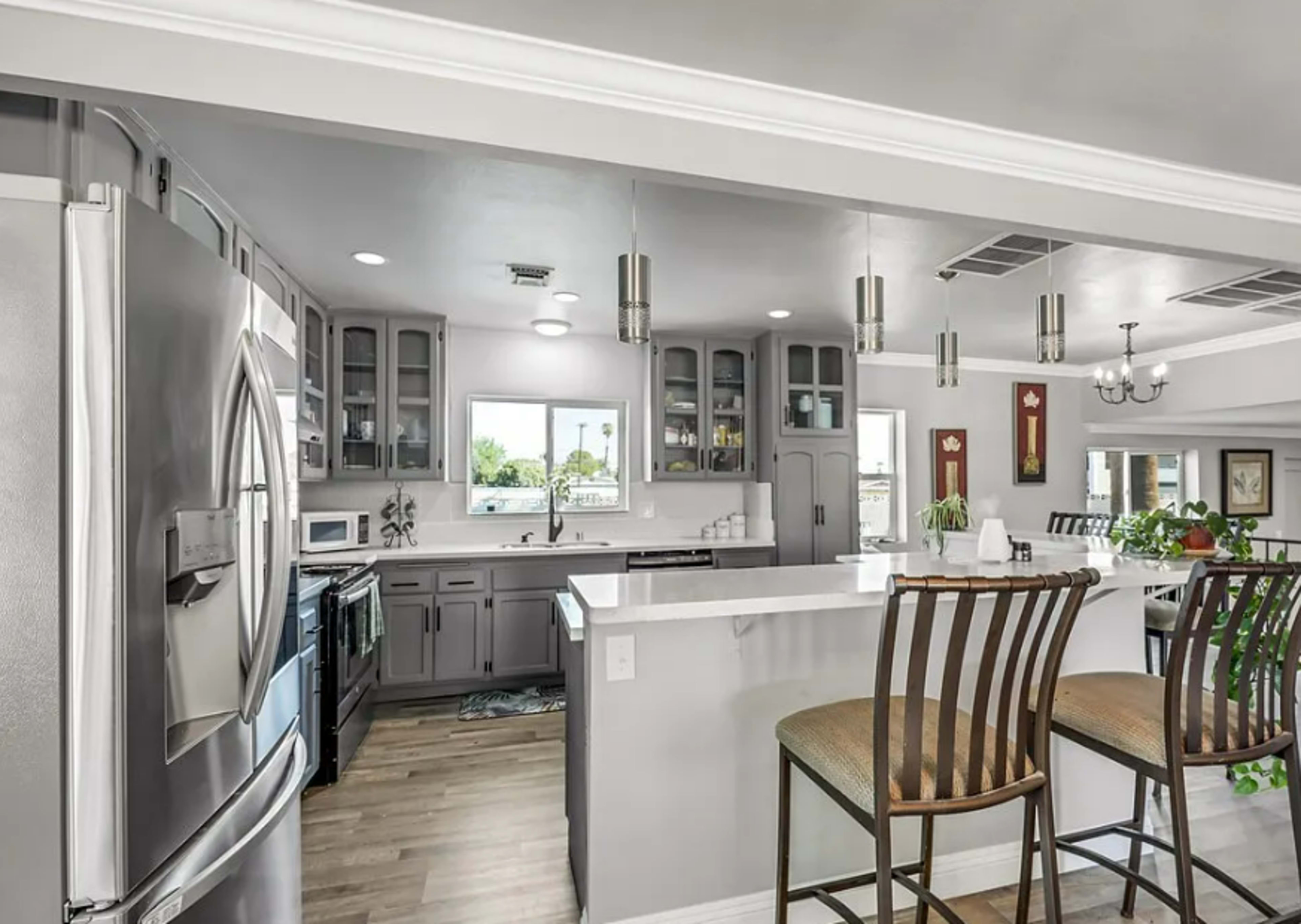 A modern kitchen features gray cabinetry, stainless steel appliances, and a breakfast bar with two stools.