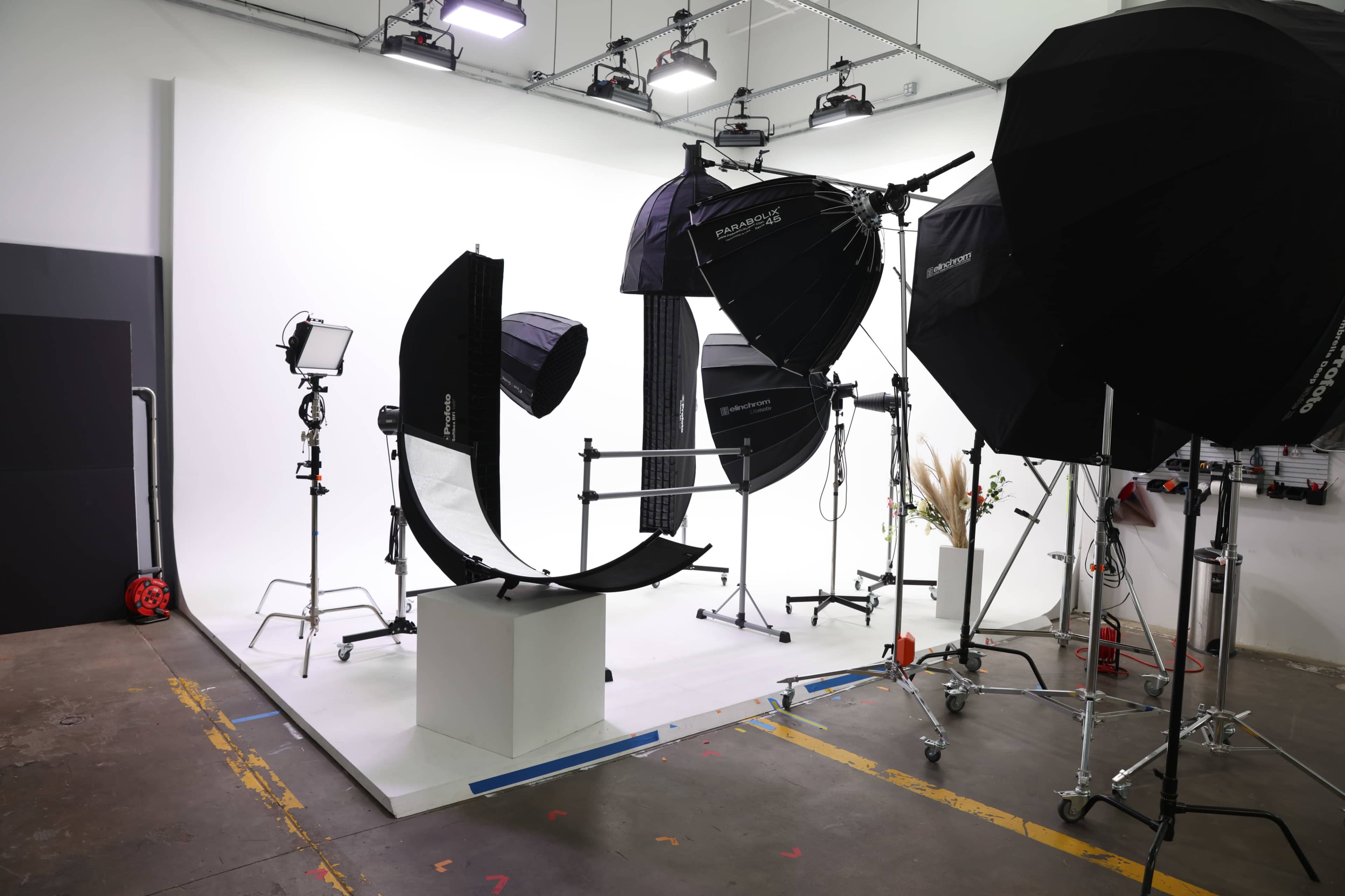 A photography studio setup with multiple light stands, softboxes, and a central display platform against a white backdrop.