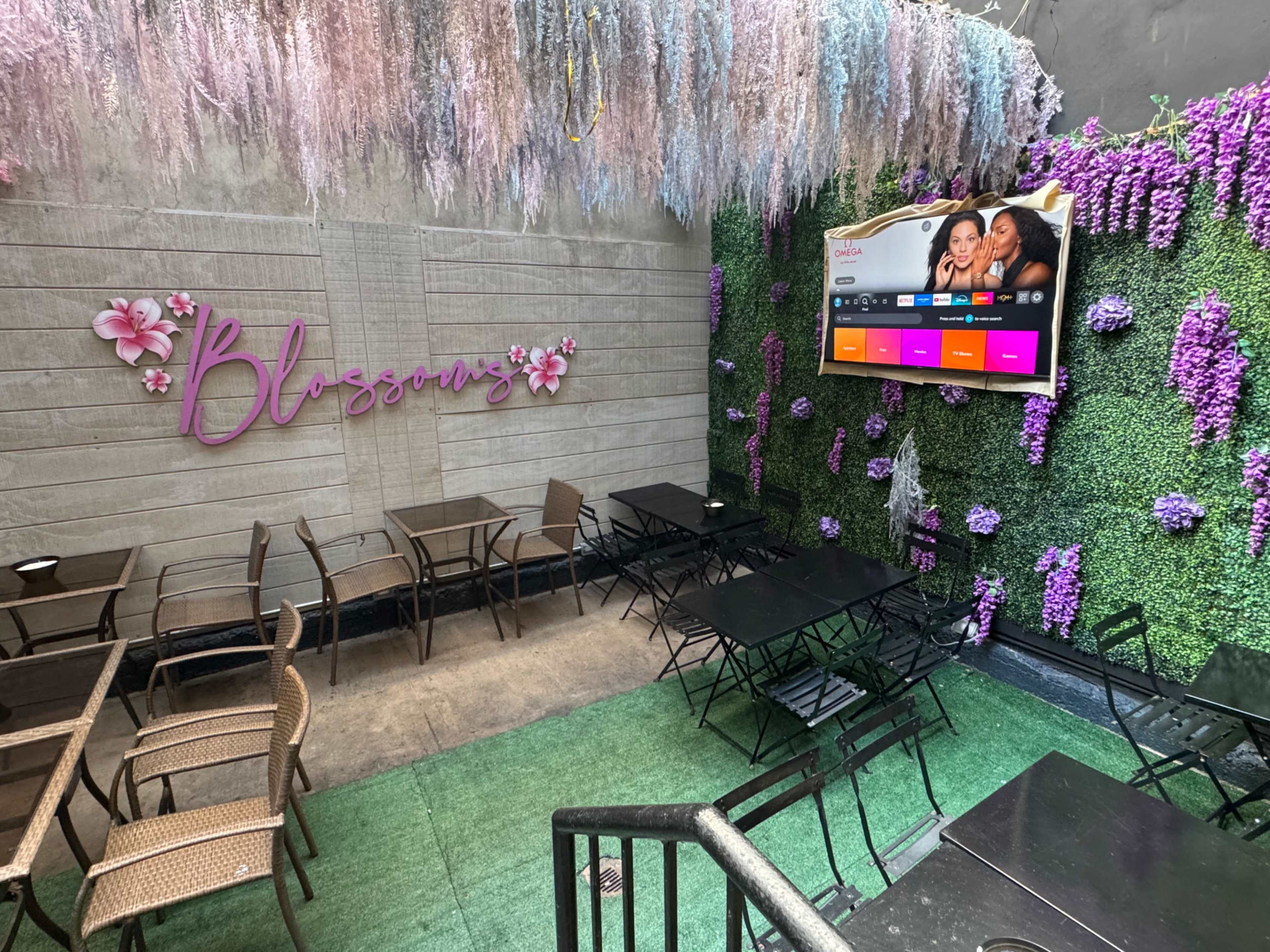 The image shows an outdoor seating area with metal chairs and tables, adorned with artificial greenery and floral decorations.