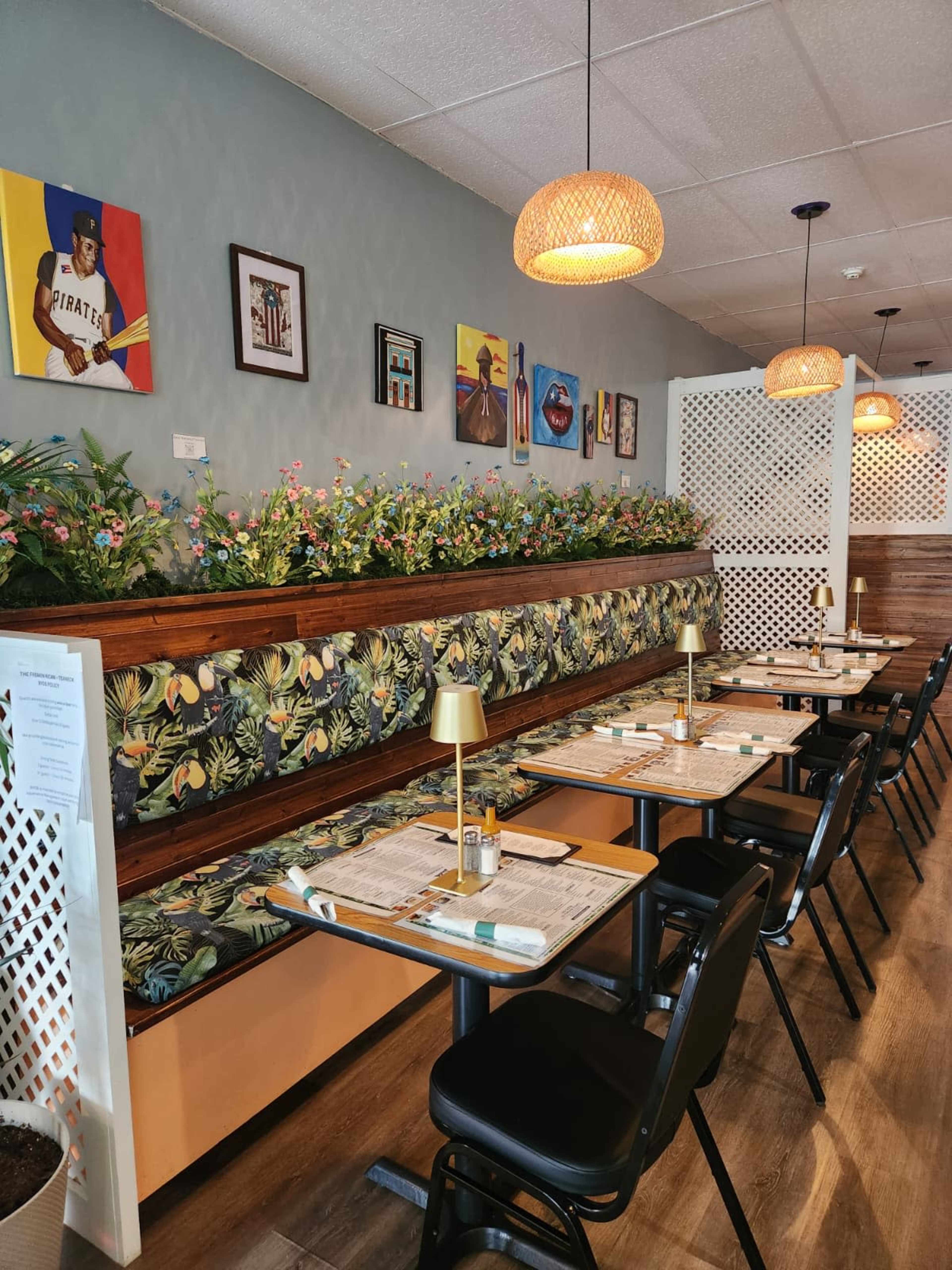 The image shows a cozy restaurant interior featuring a floral booth, wooden tables, and colorful artwork on the walls.