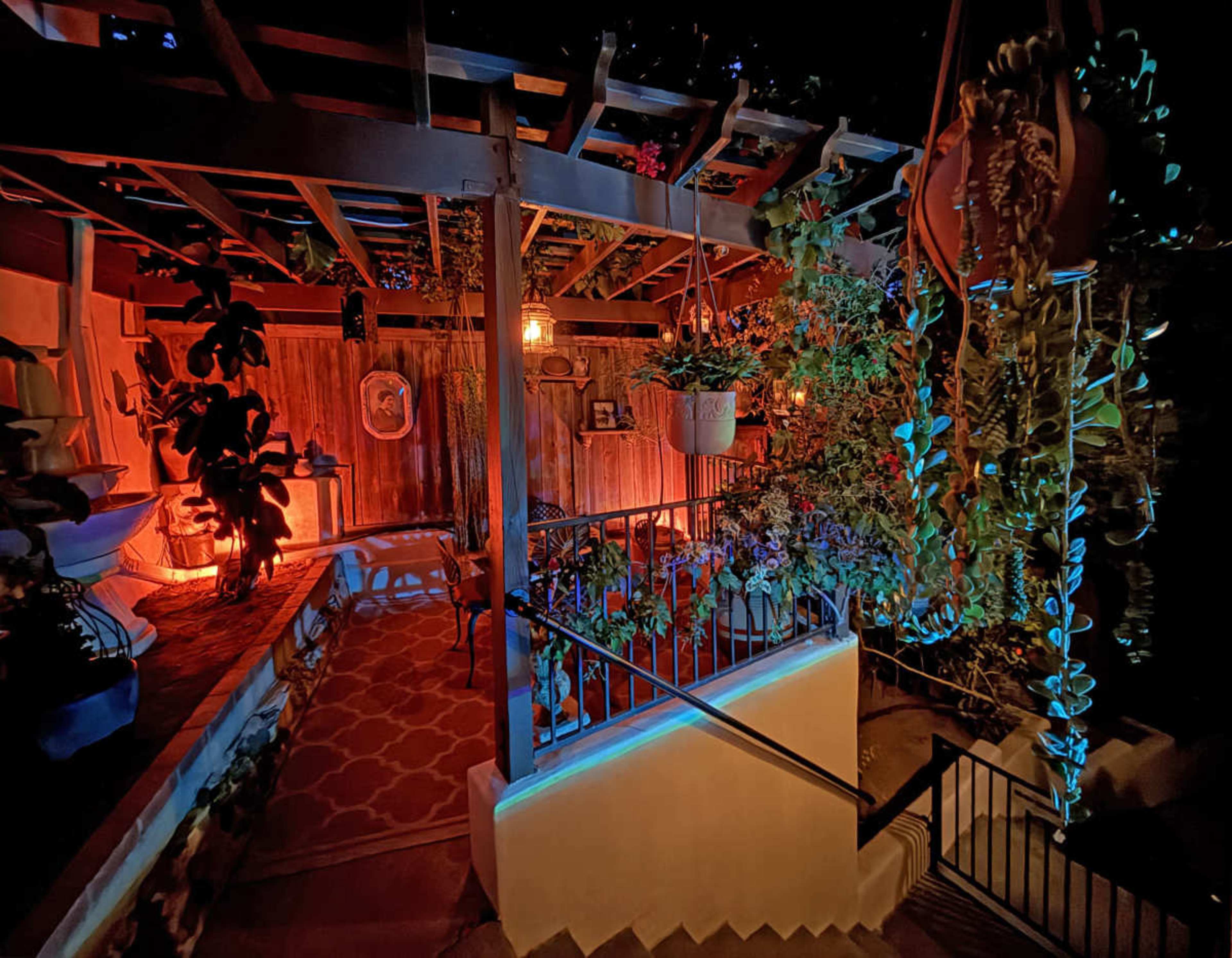 The image shows a beautifully lit outdoor patio area adorned with various plants and a staircase leading downwards.
