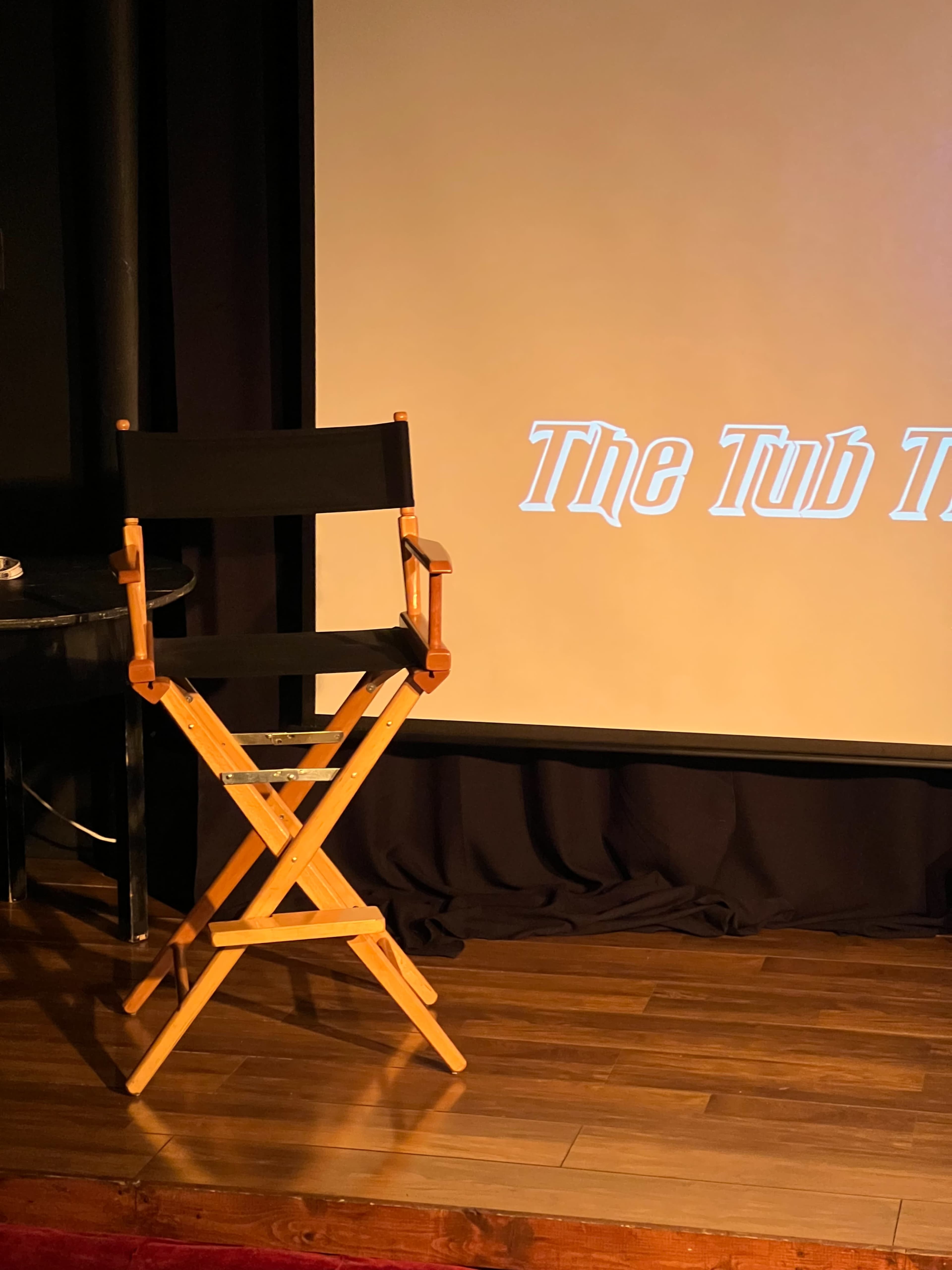 A wooden director's chair sits in front of a large screen with the words "The Tub Thumper" displayed.