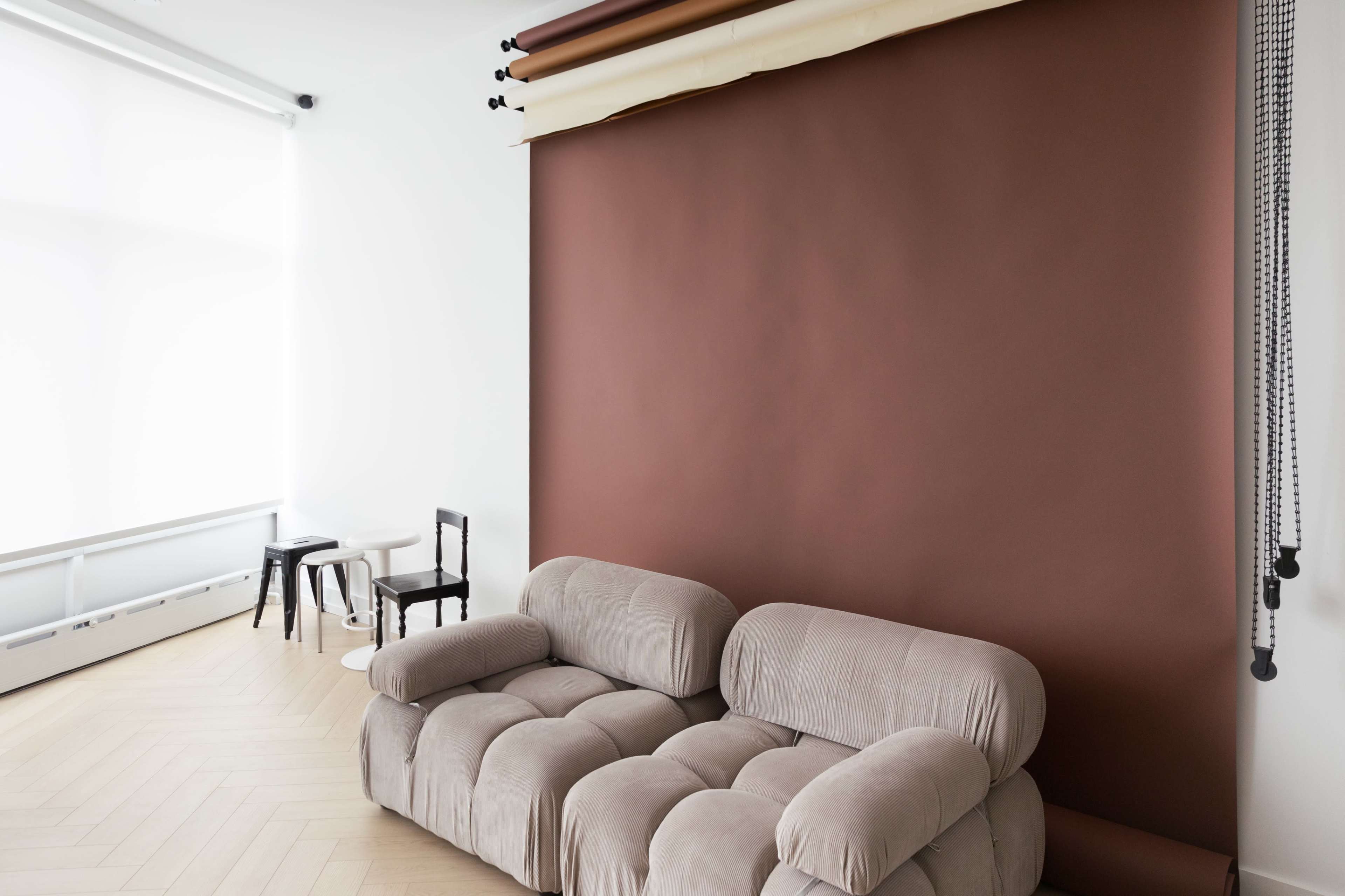 A beige sofa is positioned in front of a large brown backdrop in a minimalist room with light wooden flooring.