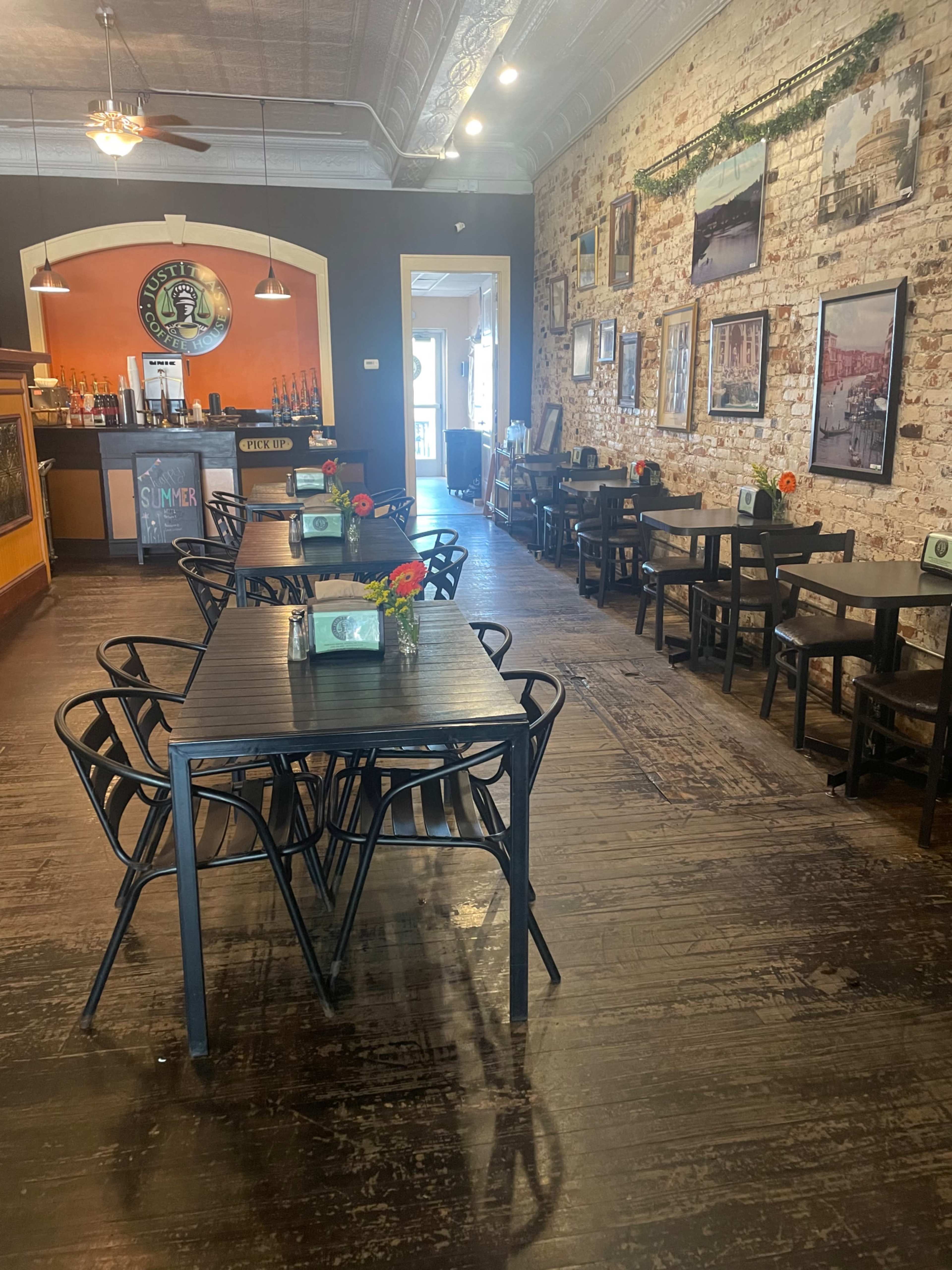 A spacious restaurant features black metal tables and chairs arranged neatly, with a bar in the background and photographs hanging on the walls.