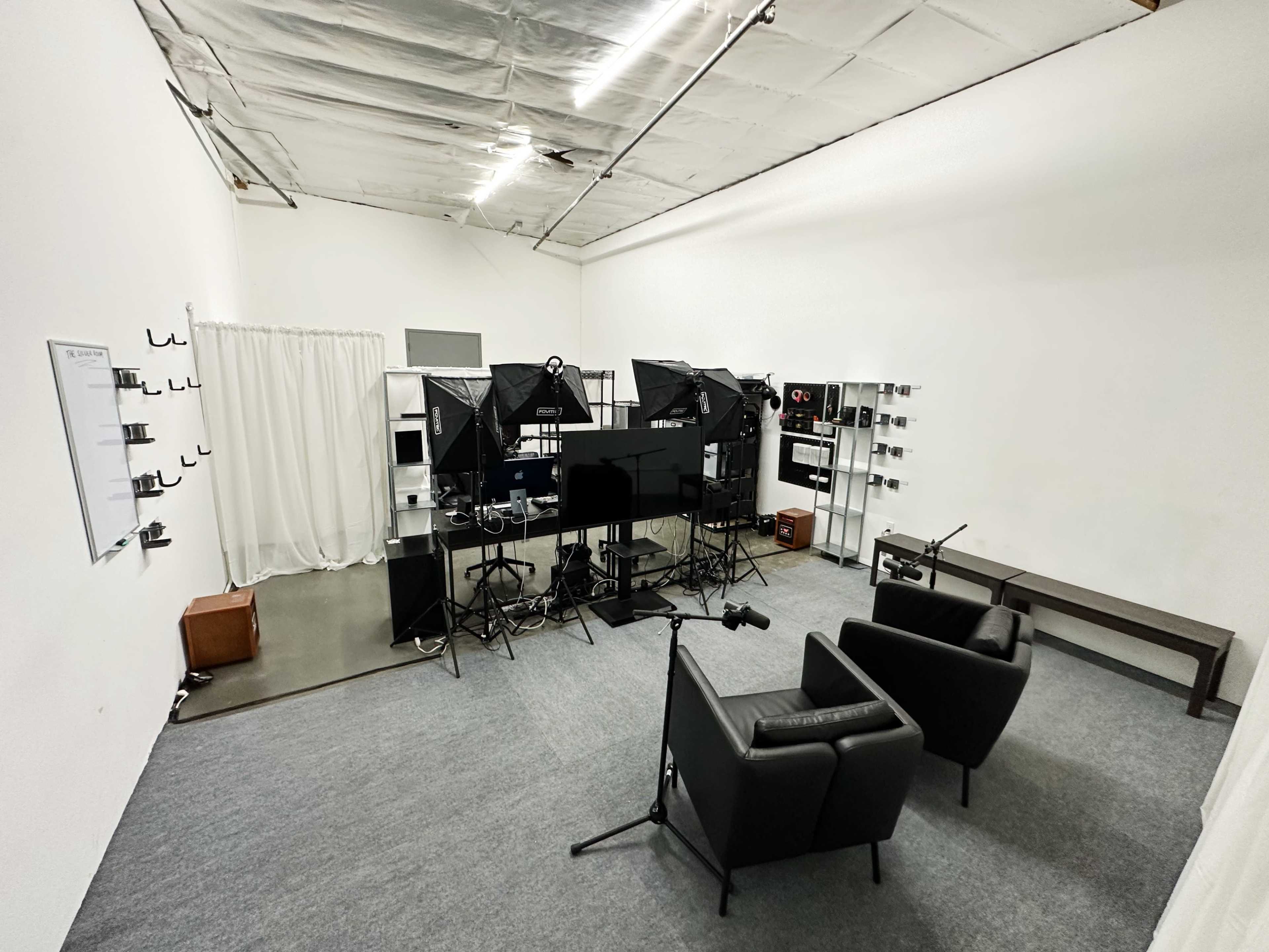 A minimalist studio setup with two black chairs, multiple lighting equipment, and a backdrop, all arranged on gray carpeting.