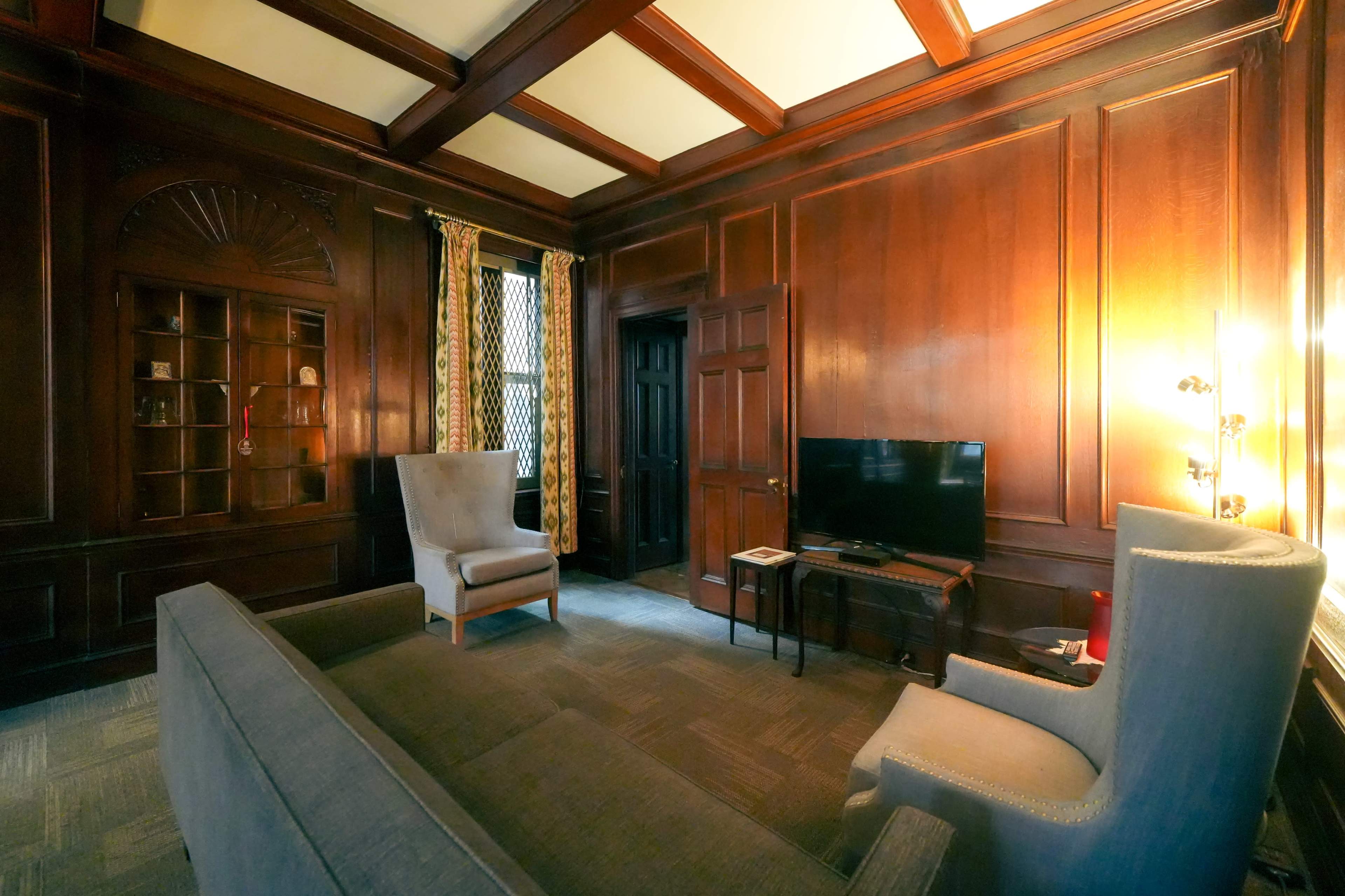 The image shows a wooden-paneled room with a sofa, two armchairs, a television, and a lighted corner table.