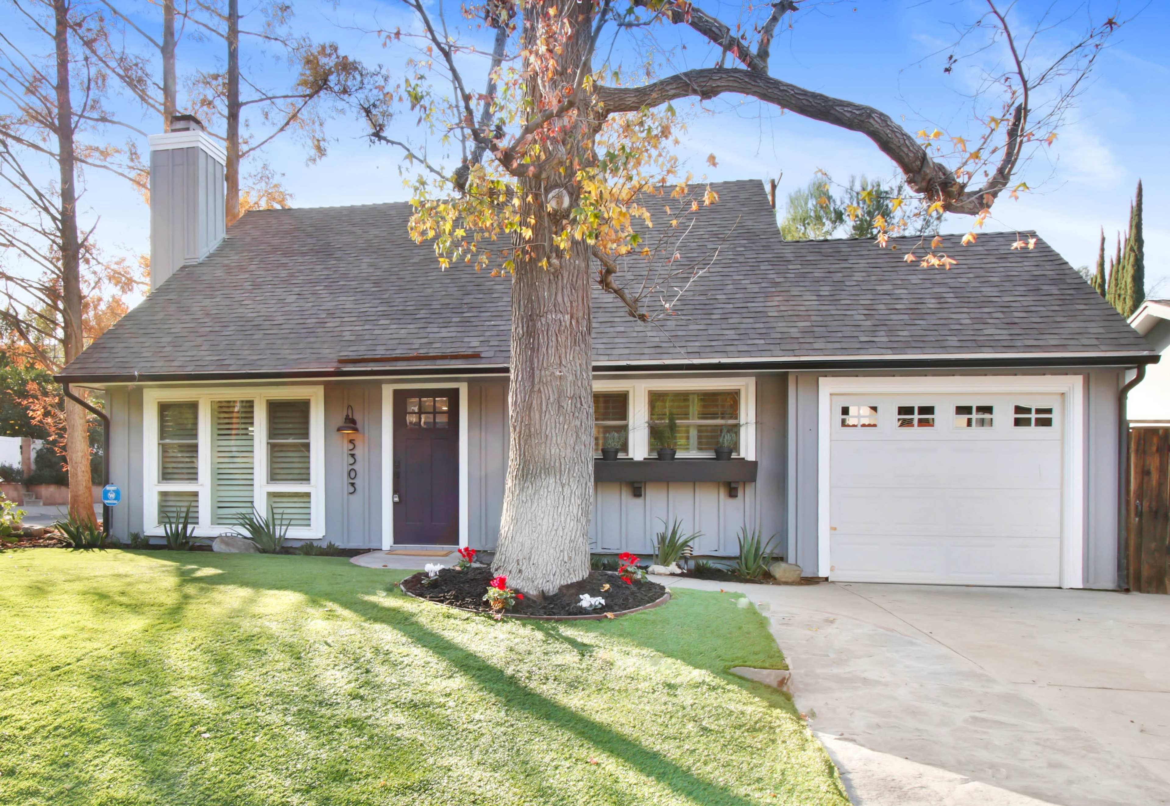 A single-story house with a pitched roof, a front yard featuring grass and flower beds, and a garage on the right.