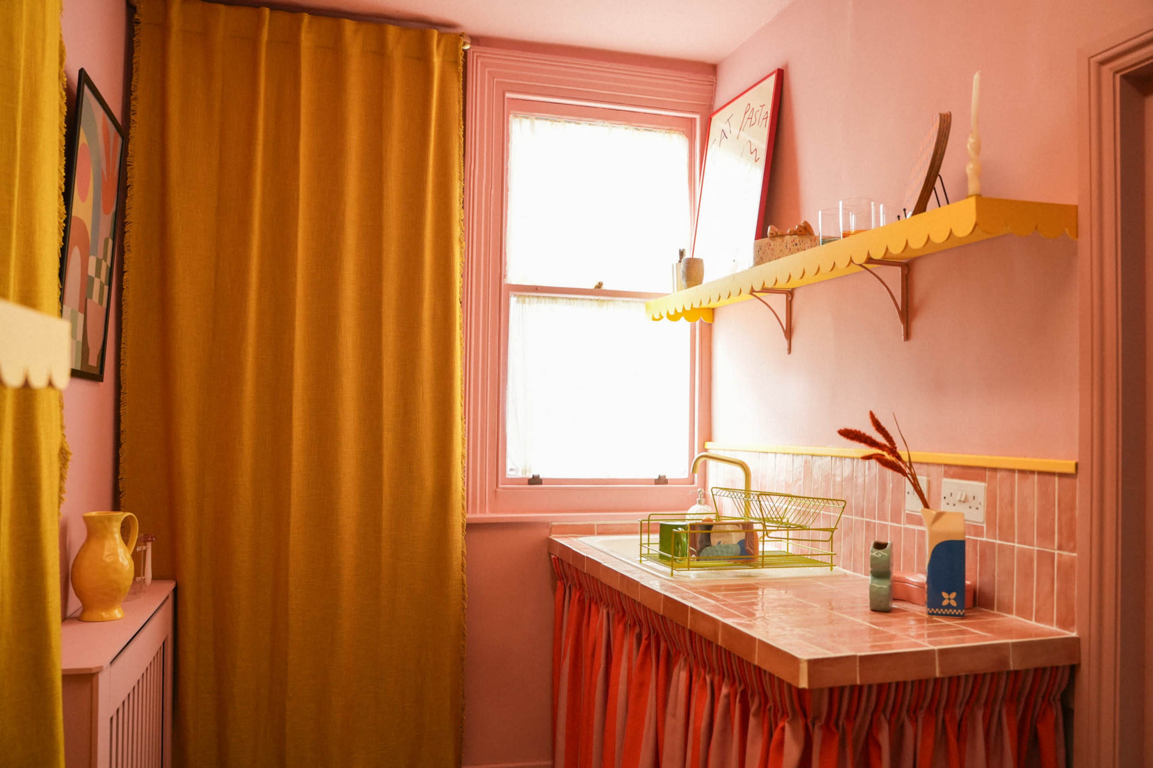 The image shows a brightly colored bathroom with pink walls, a yellow curtain, and a pink countertop adorned with a green basket and decorative items.