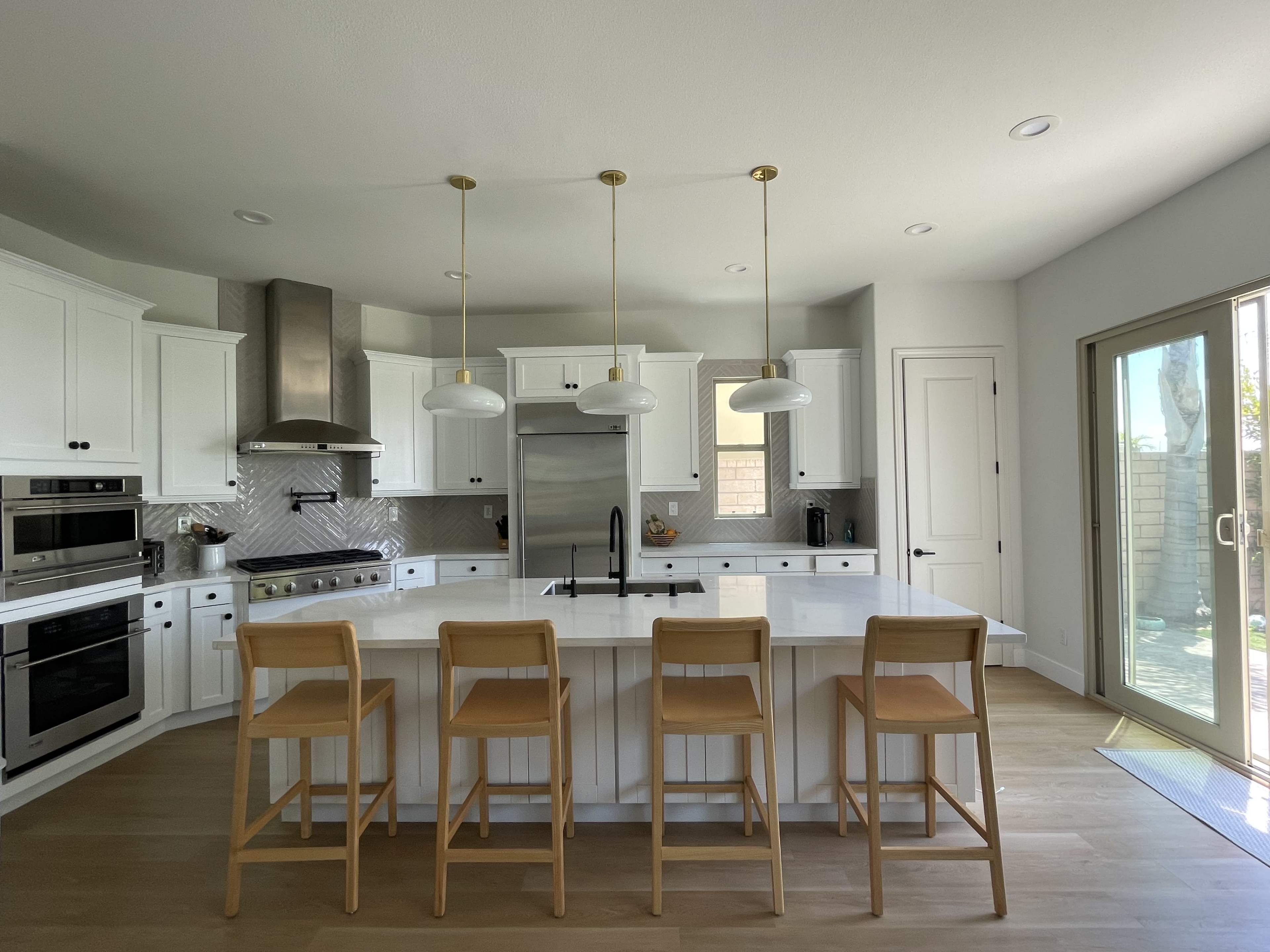 A modern kitchen features white cabinetry, stainless steel appliances, and a large island with four wooden bar stools.