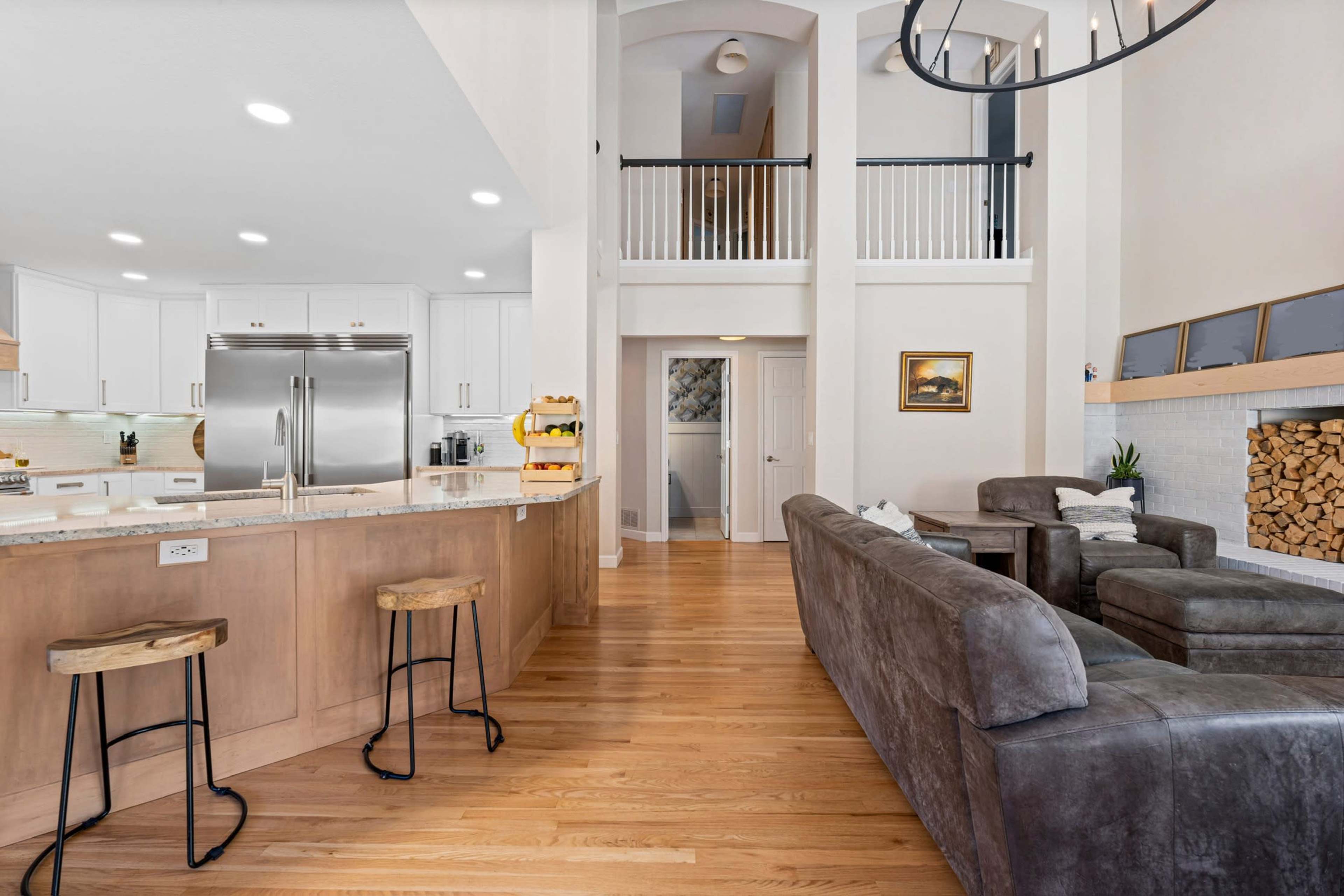 The image features a modern open-concept kitchen and living area with a large island, bar stools, and a stacked wood fireplace.