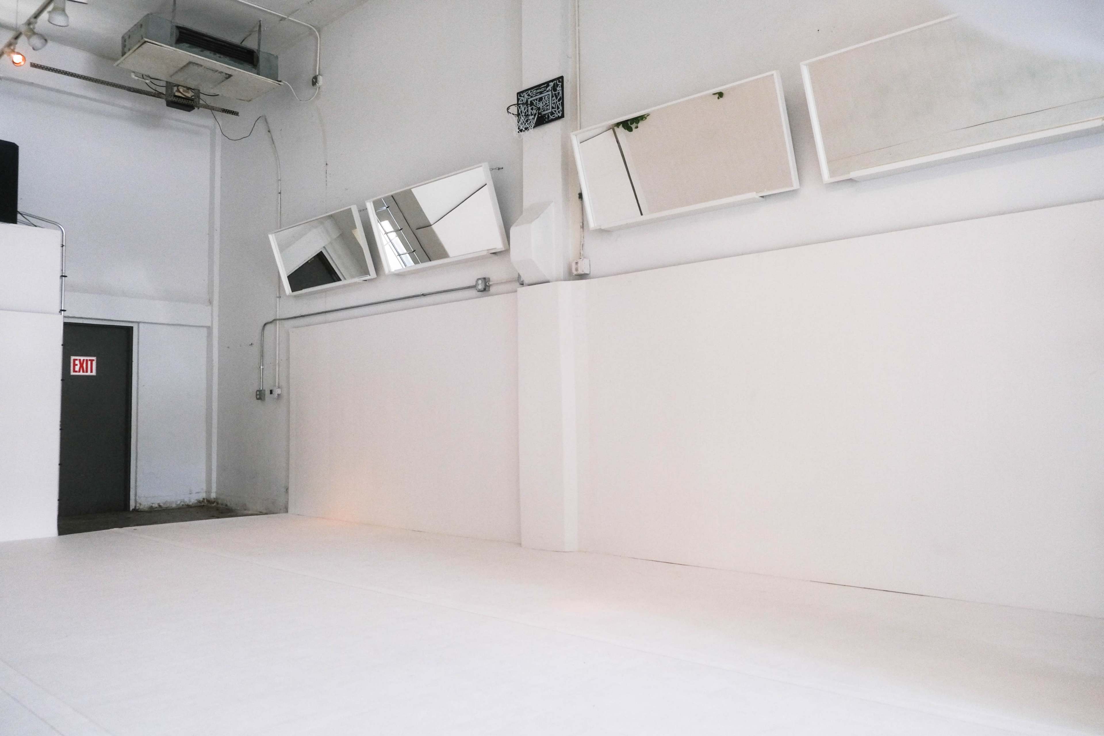 A minimalistic, empty room with white walls and mirrors mounted on one side.